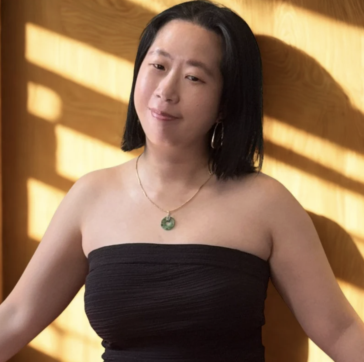A young woman with long dark hair looking out a window in a modern building, smiling softly.