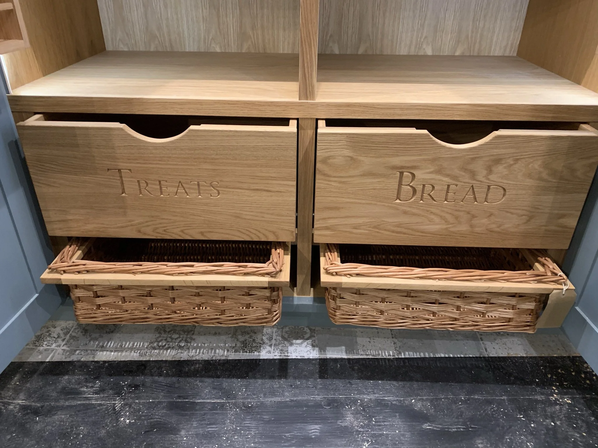 Part of a Marc Smith bespoke kitchen pantry featuring wicker baskets and personalised carving on the wooden drawers.