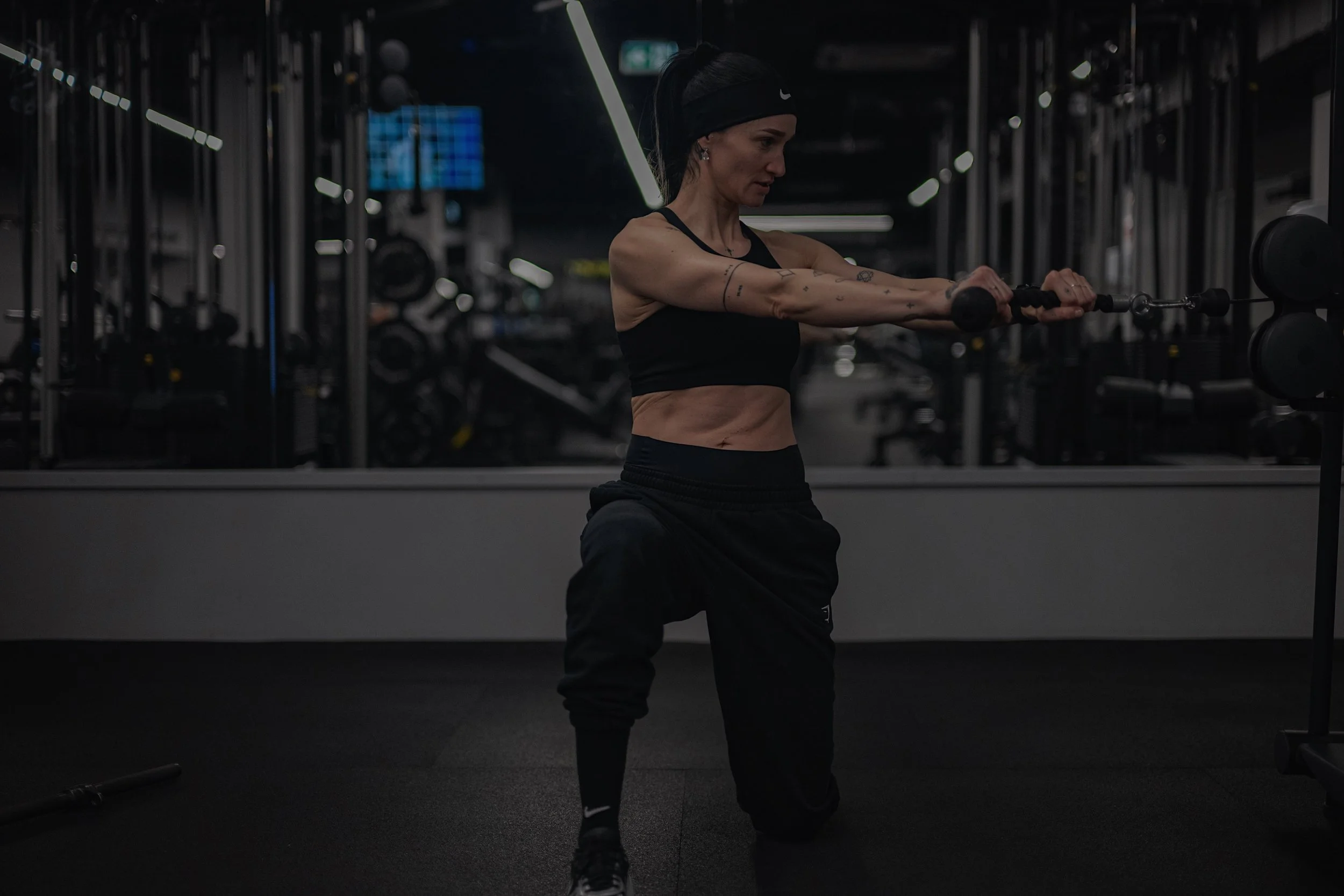Woman exercising in gym, using cable machine, wearing black sportswear.