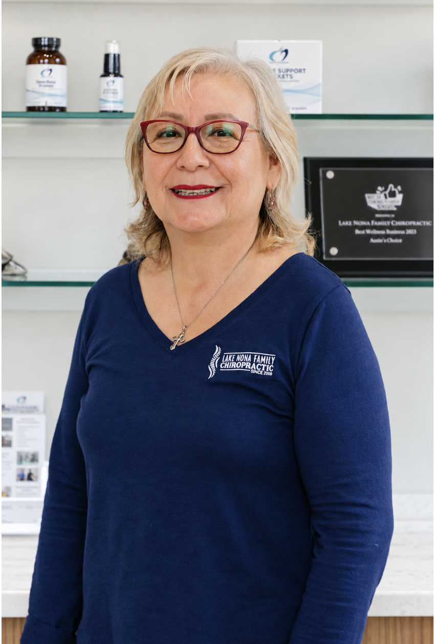 A woman with shoulder-length reddish-brown hair and red glasses, wearing a black long-sleeve shirt with a logo on the left chest that reads 'Lake Nona Family Chiropractic since 2013.'