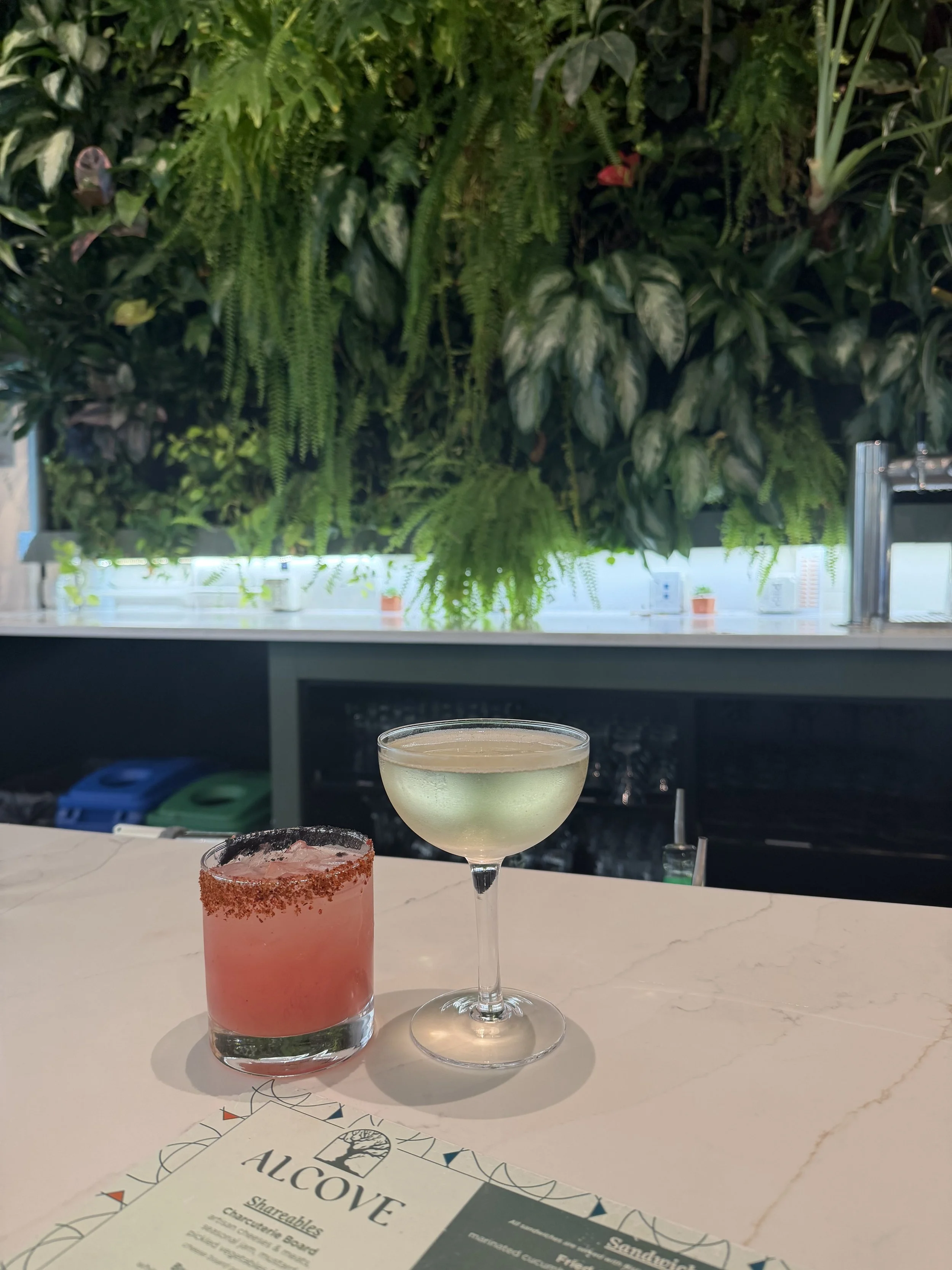 Two cocktails on a marble bar beneath a living plant wall