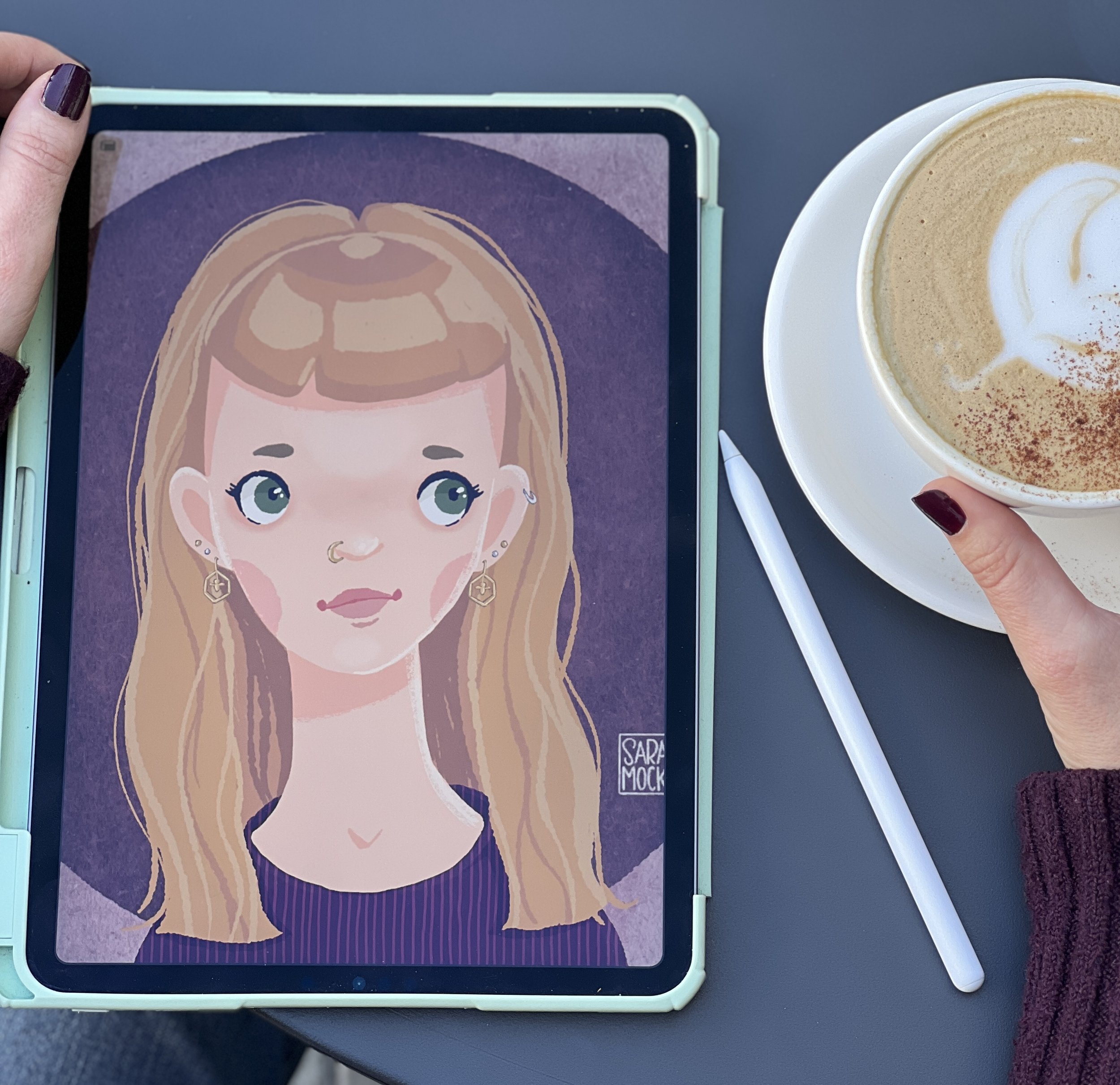 A digital drawing of a girl with large green eyes, blonde hair, and earrings on a device screen, with a beverage cup beside it.