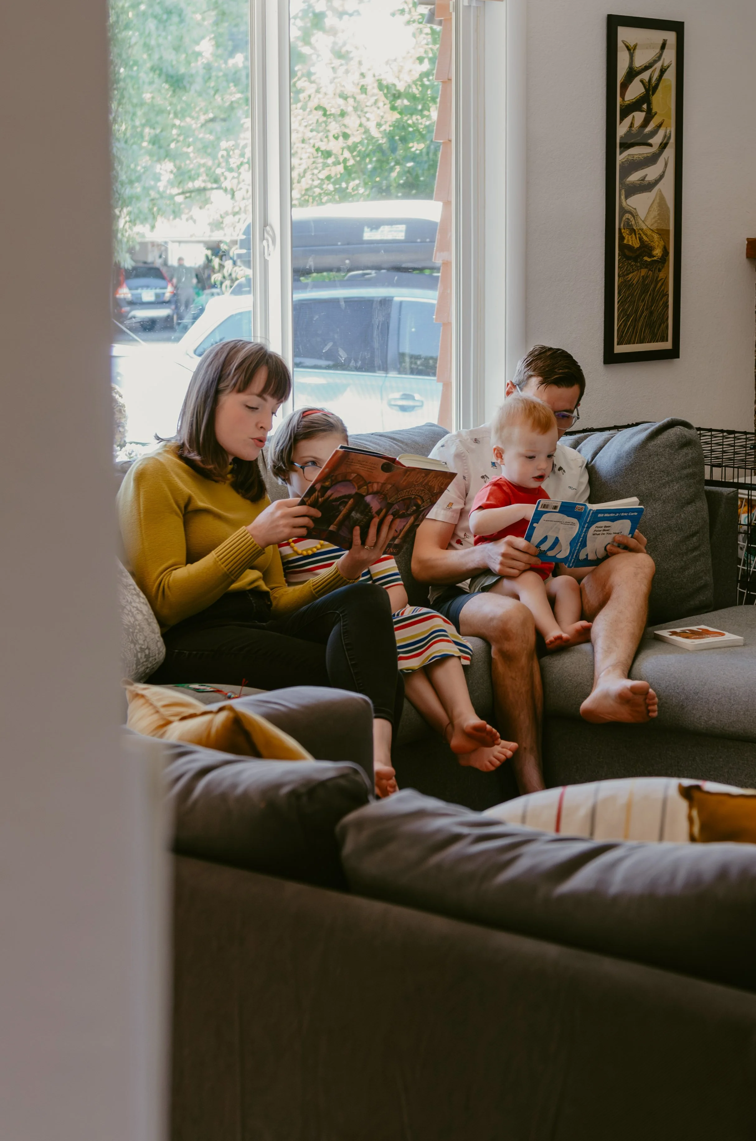 An at home lifestyle family photography session in Salem Oregon of parents and kids reading on the couch by the window