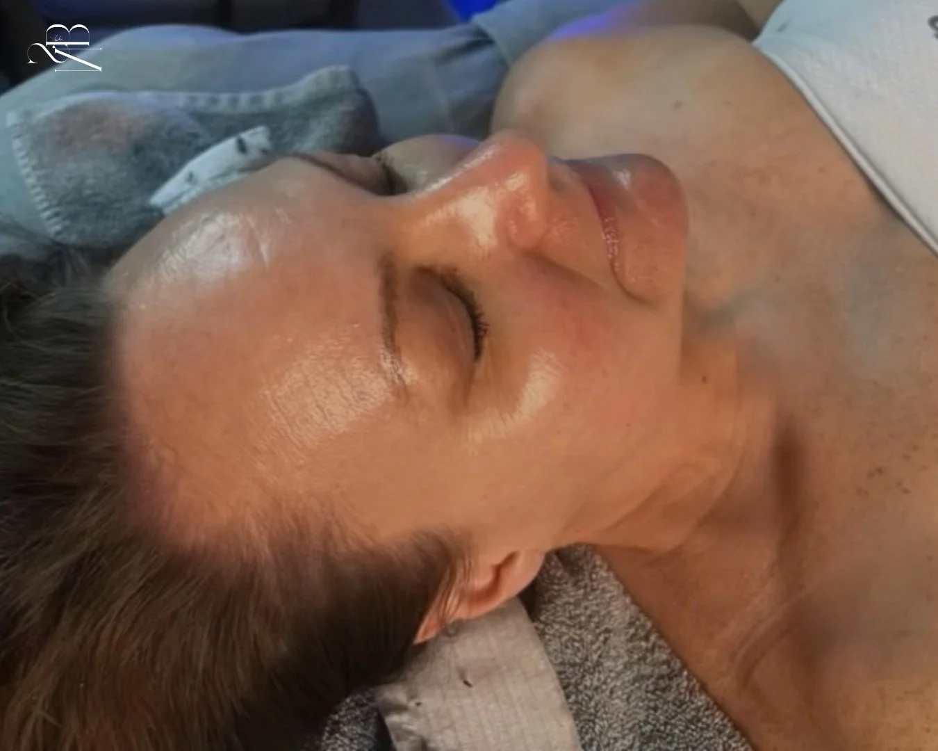 A woman lying on her side with eyes closed, showing her relaxed face and tousled brown hair.