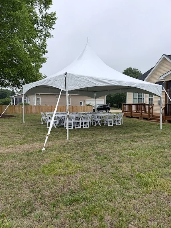 20x20' high peak tent installed on grass with white tables and chairs underneath