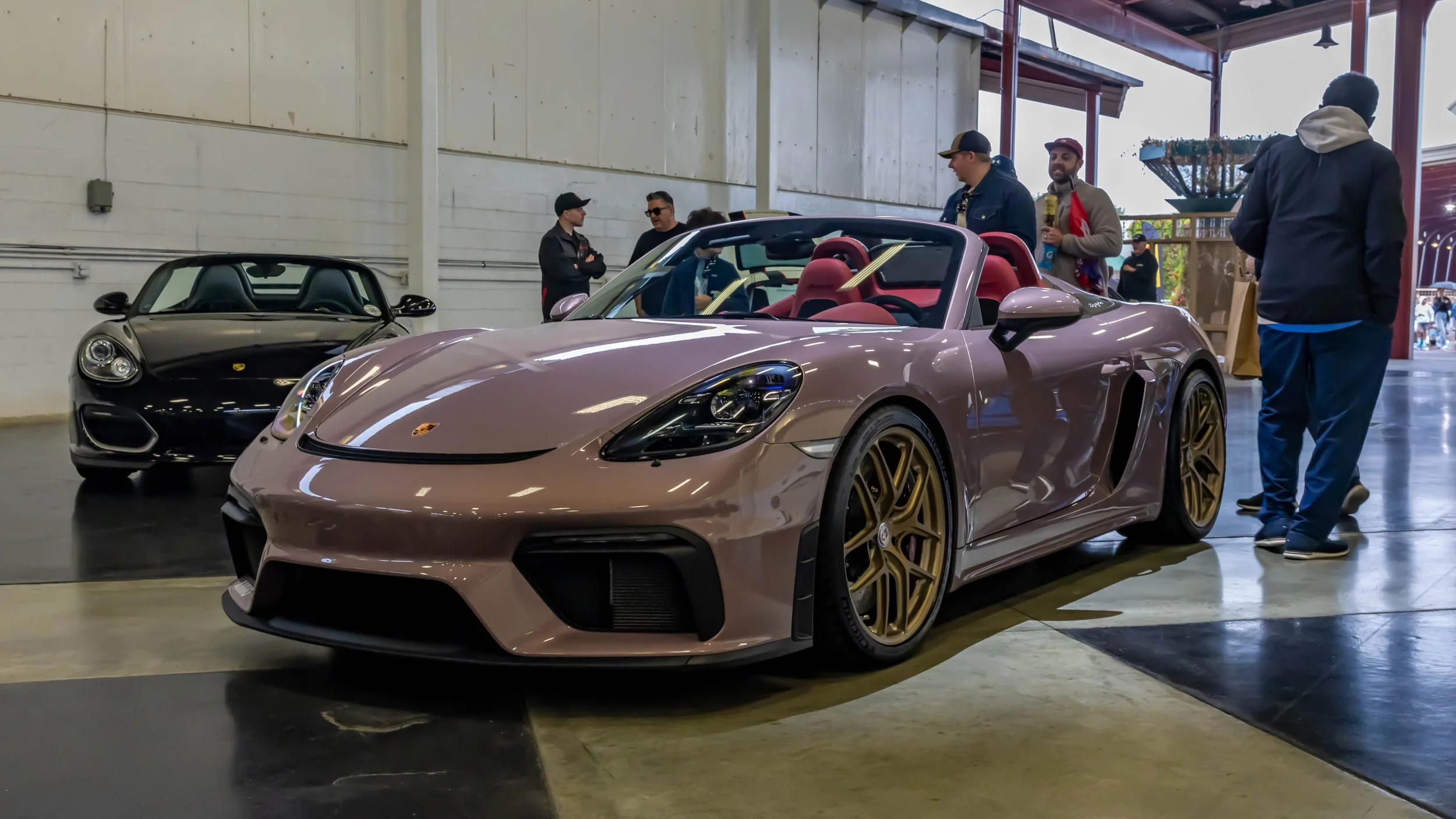 Air | Water 2025 — Orange County Fairgrounds — A low-angle, front three-quarter view of Matt Farah's Frozen Berry Metallic Porsche 718 Spyder with a red leather interior. The car is fitted with bronze HRE multi-spoke wheels and is displayed indoors o