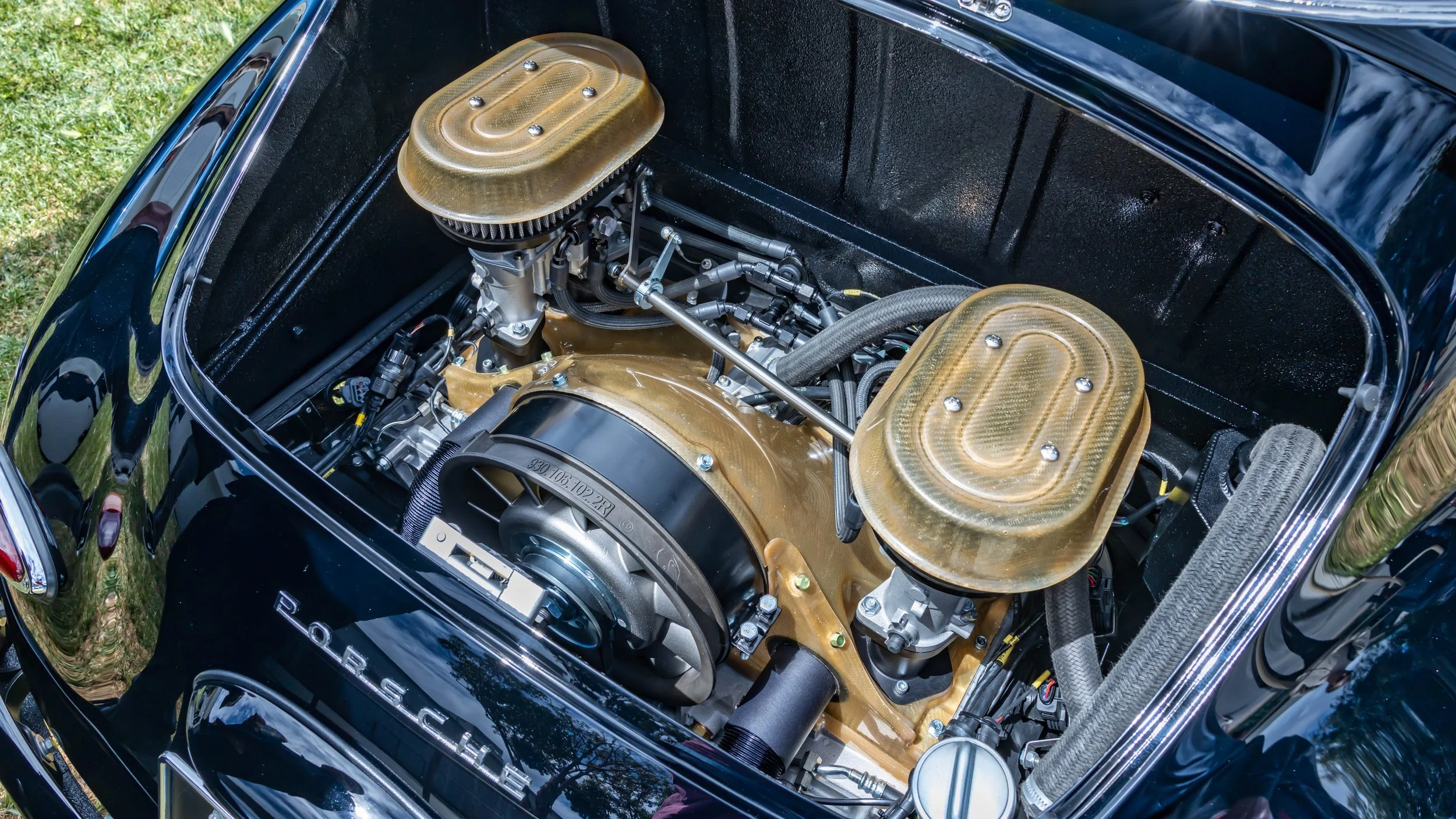 Air | Water 2025 — Emory Motorsports — OC Fairgrounds — A high-angle view into the meticulously prepared engine bay of a classic black Porsche 356 Emory Outlaw, showcasing a highly modified Emory-Rothsport Outlaw-4 air-cooled engine. The engine featu