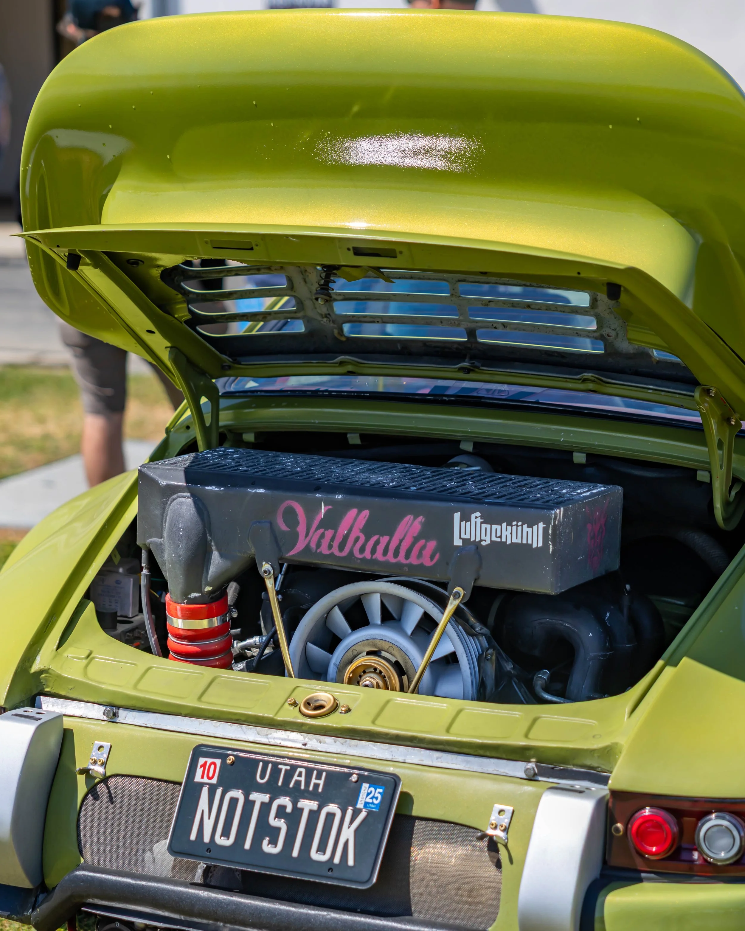 Air | Water 2025 — Orange County Fairgrounds — A high-angle, close-up view of the rear of a classic Porsche 911 in a metallic lime green finish. The engine lid is propped open, showcasing a modified air-cooled engine with a prominent cooling fan. A b