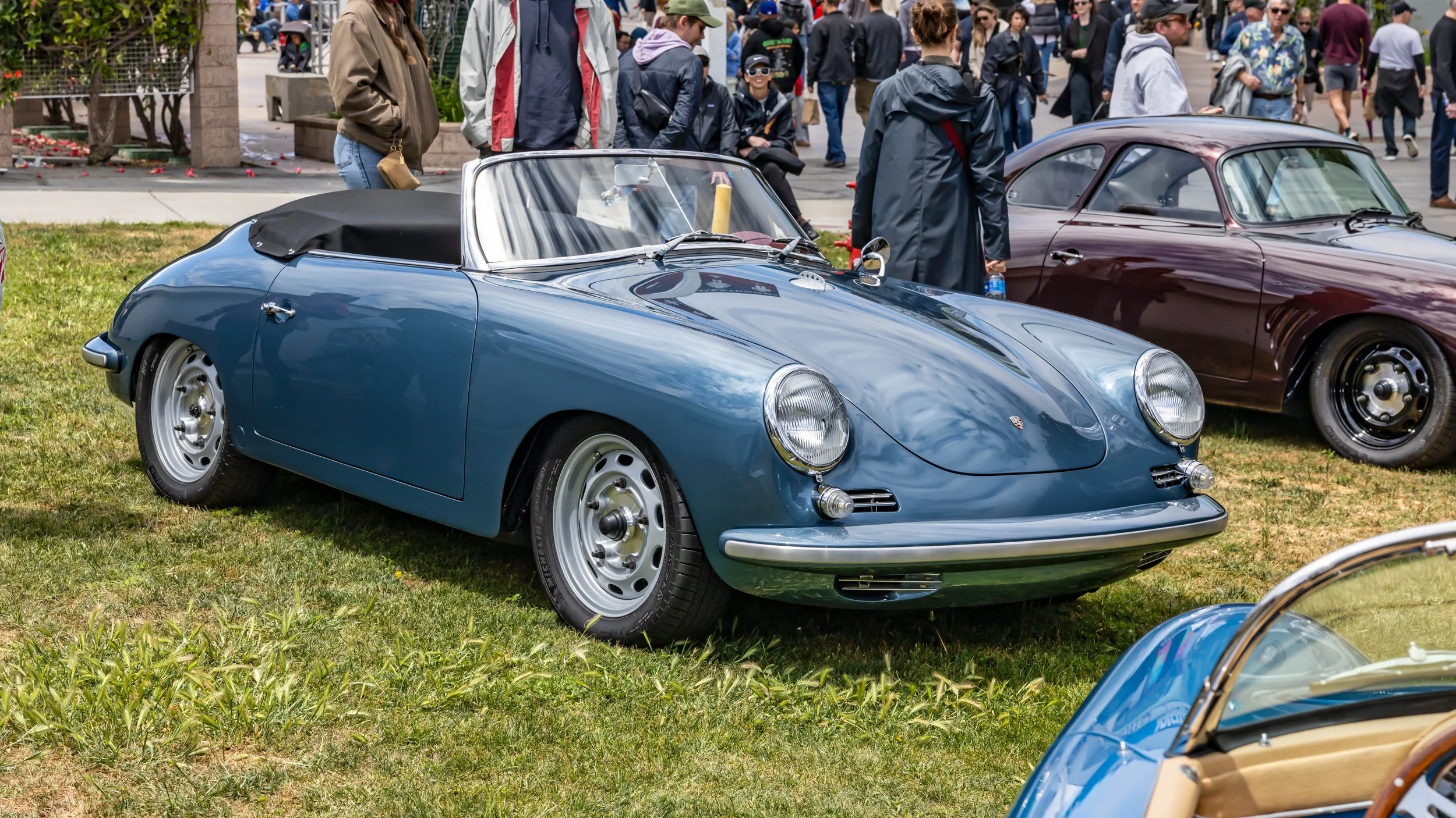 Air | Water 2025 — Emory Motorsports — OC Fairgrounds — A classic blue Porsche 356 A Emory Speedster with a black soft top is parked on a grassy lawn at an outdoor car show. The car features silver vented steel-style wheels and a low-cut windshield. 