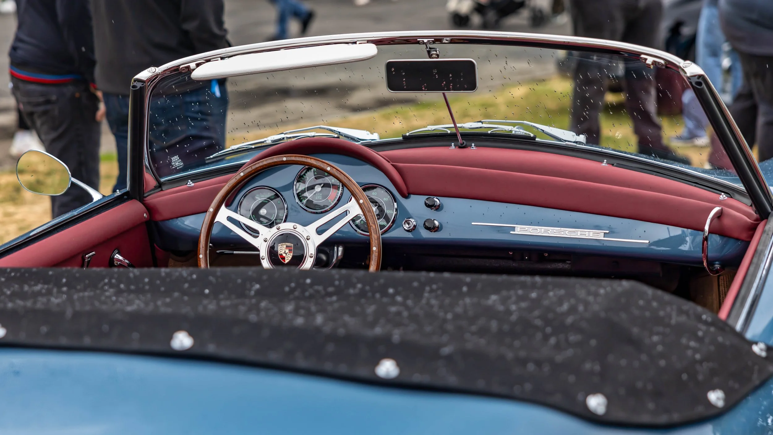 Air | Water 2025 — Emory Motorsports — OC Fairgrounds — A close-up view into the cockpit of a classic light blue Porsche 356 Emory Speedster, featuring a striking red leather interior. The wood-rimmed, three-spoke steering wheel with the Porsche cres