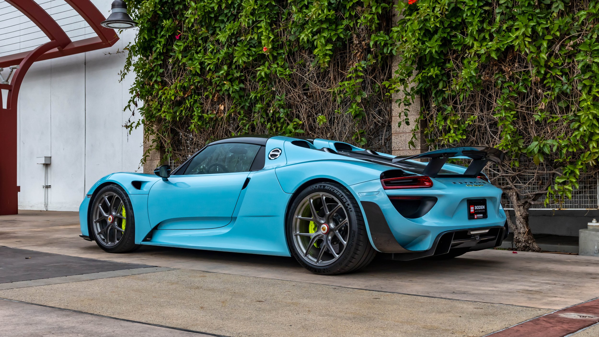 Air | Water 2025 — Orange County Fairgrounds — A rear three-quarter view of a light blue Porsche 918 Spyder with the Weissach Package, parked on a concrete driveway. The car features a prominent carbon-fiber rear wing, magnesium center-lock wheels, a
