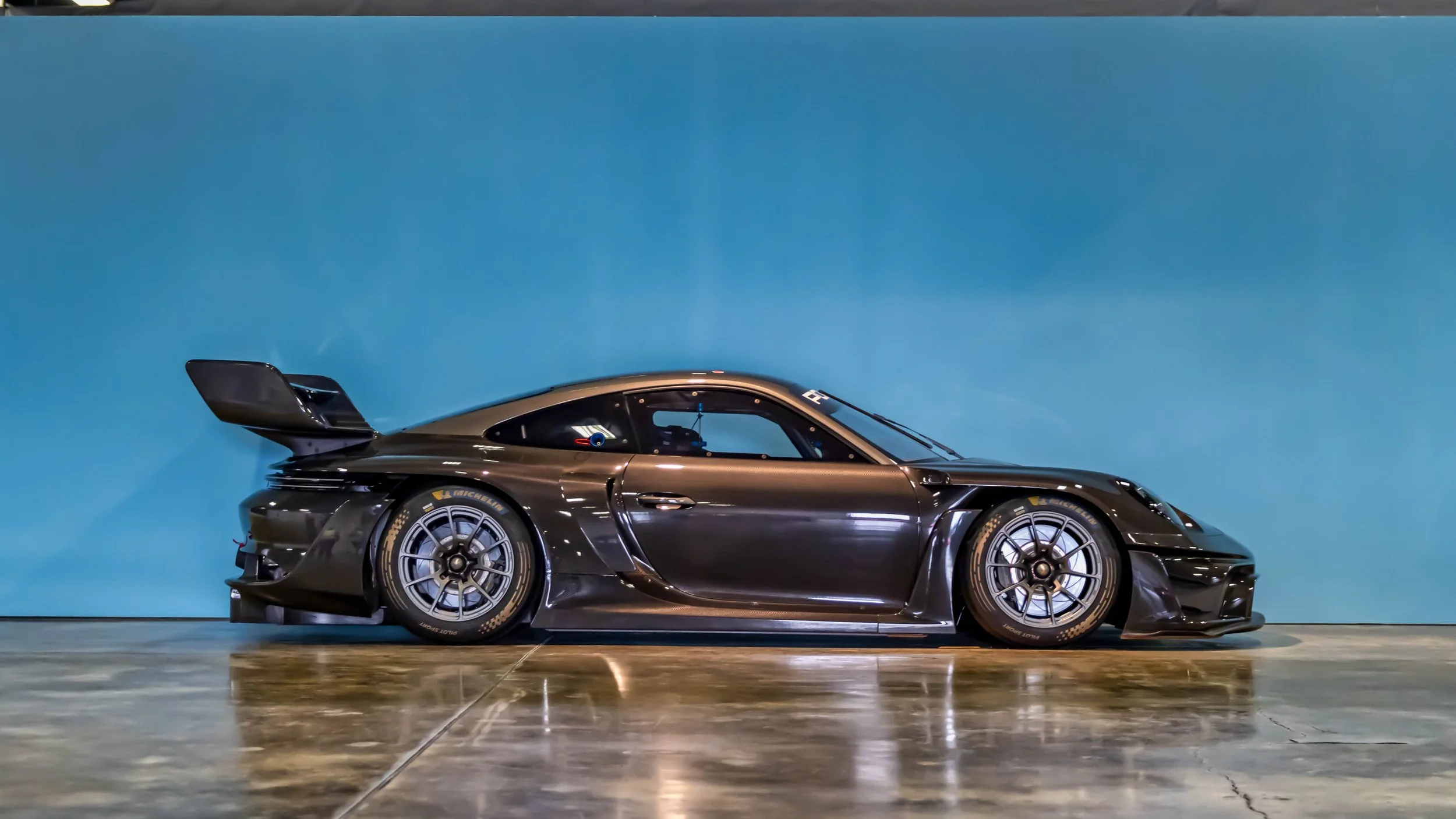 Air | Water 2025 — Orange County Fairgrounds — A side profile view of a Porsche 911 GT2 RS Clubsport 25 track car,  finished in dark grey. The car features aggressive aerodynamics, including a large swan-neck rear wing, wide fenders, and is fitted wi