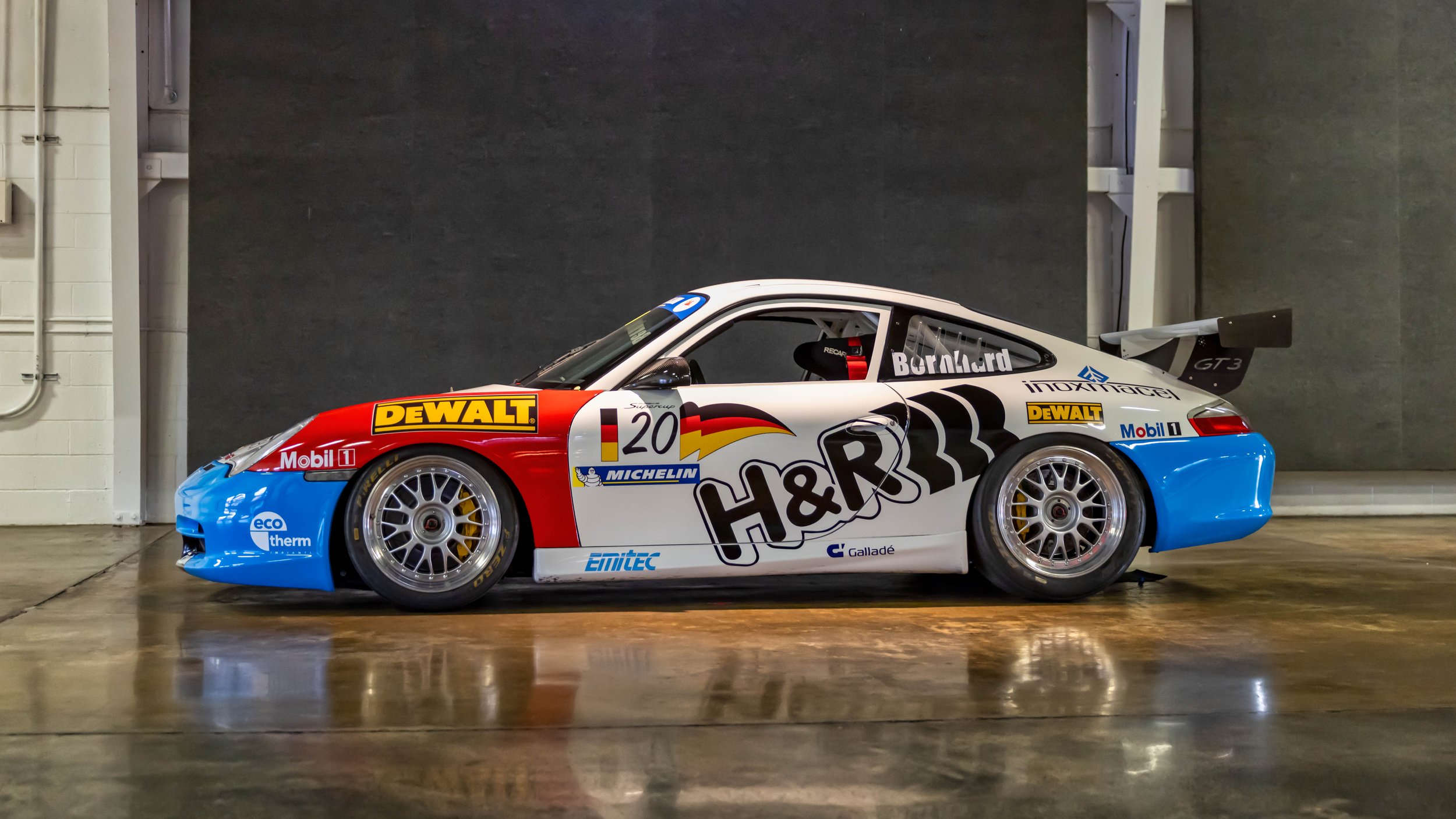 Air | Water 2025 — Orange County Fairgrounds — A Porsche 911 GT3 Cup (996) race car, presented in a full side profile. The car features a prominent white, red, and blue livery with numerous sponsor decals, including H&R, DEWALT, and Mobil 1. It is pa