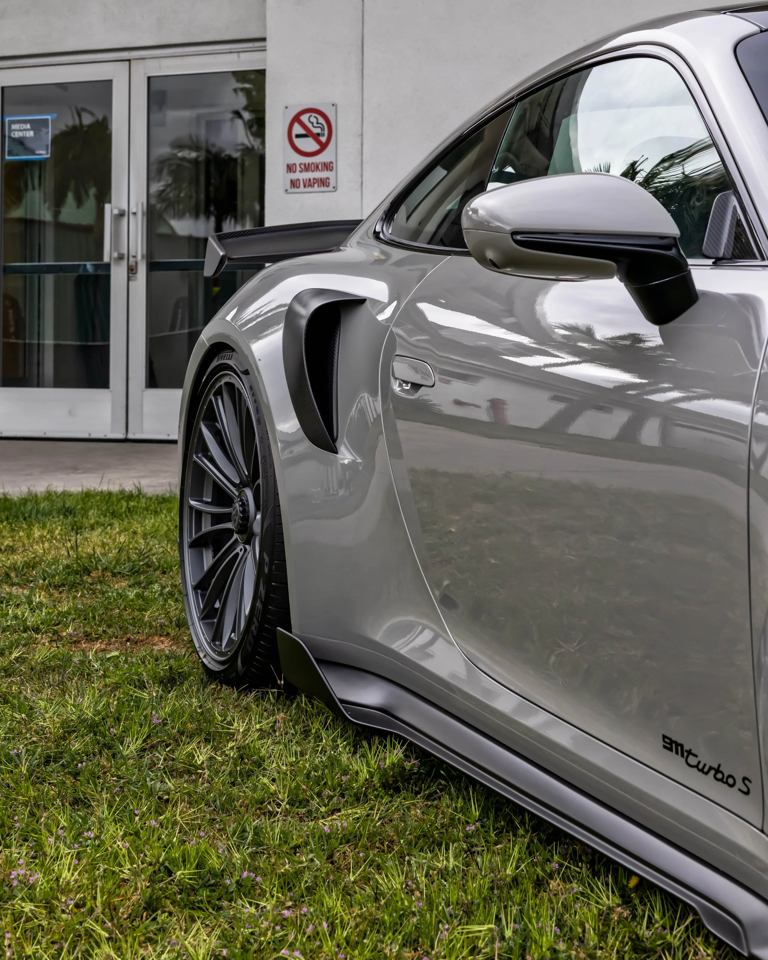 Air | Water 2025 — Gunther Werks — Orange County Fairgrounds — A low-angle, side profile view of a Chalk Grey Porsche 992 911 Turbo S parked on a green lawn. The shot focused on the GW9 carbon-fiber aero air foilers, aero side intake scoops, side aer