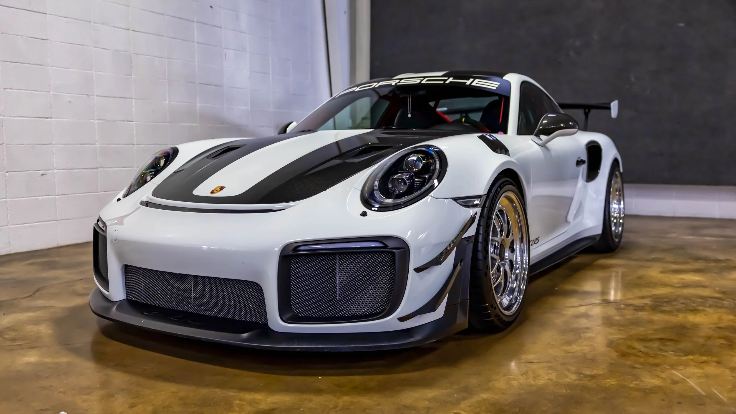 Air | Water 2025 — Orange County Fairgrounds — A white Porsche 911 GT2 RS (991.2) is parked indoors on a polished concrete floor. The car features extensive carbon-fiber components, including the hood, front fender vents, and side mirrors, along with