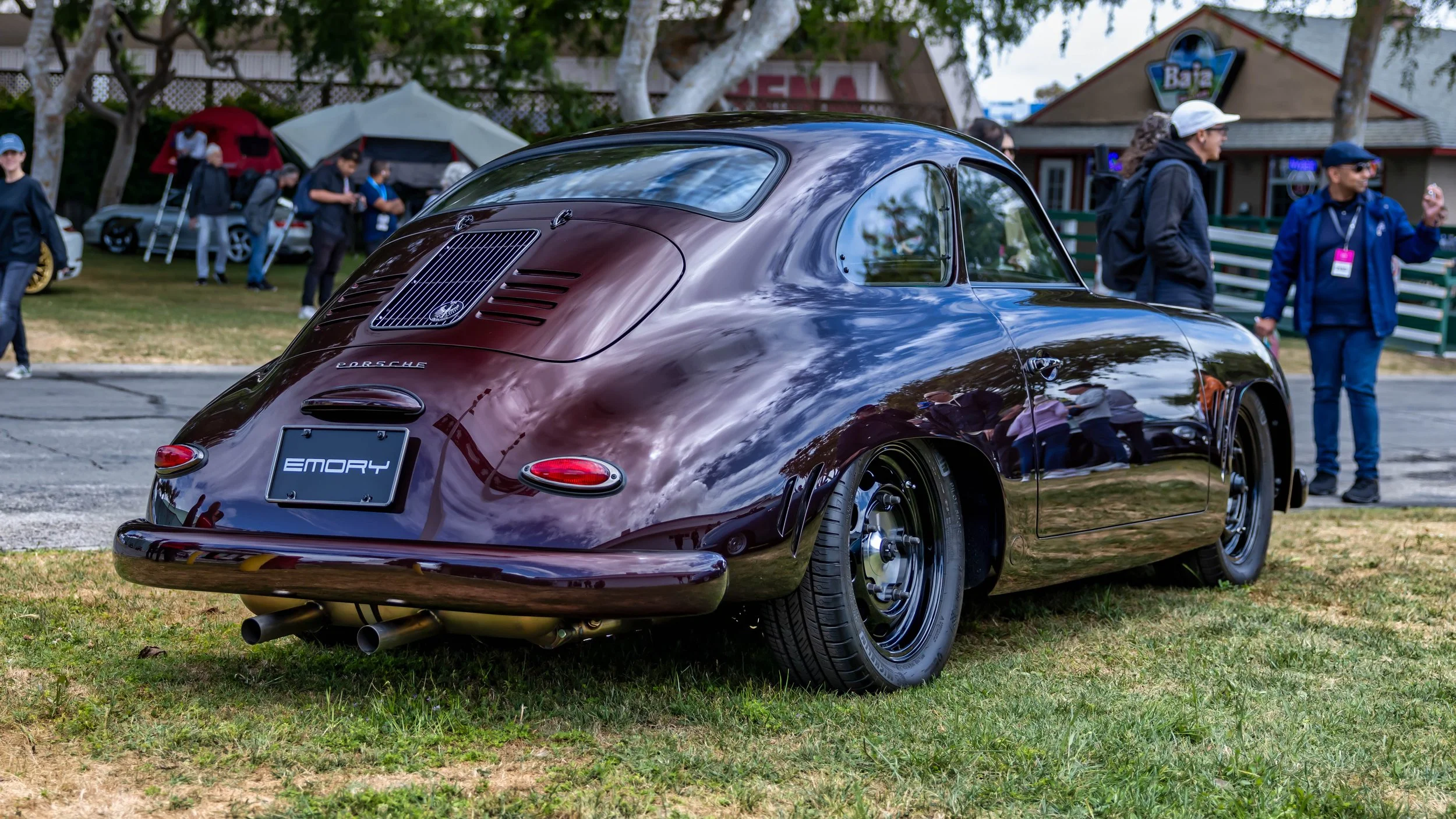 Air | Water 2025 — Emory Motorsports — OC Fairgrounds — A rear three-quarter view of a custom Porsche 356 Emory Outlaw Special coupe, finished in a Superior Red Metallic paint. The car is parked on a grassy lawn at an outdoor car show, showcasing its