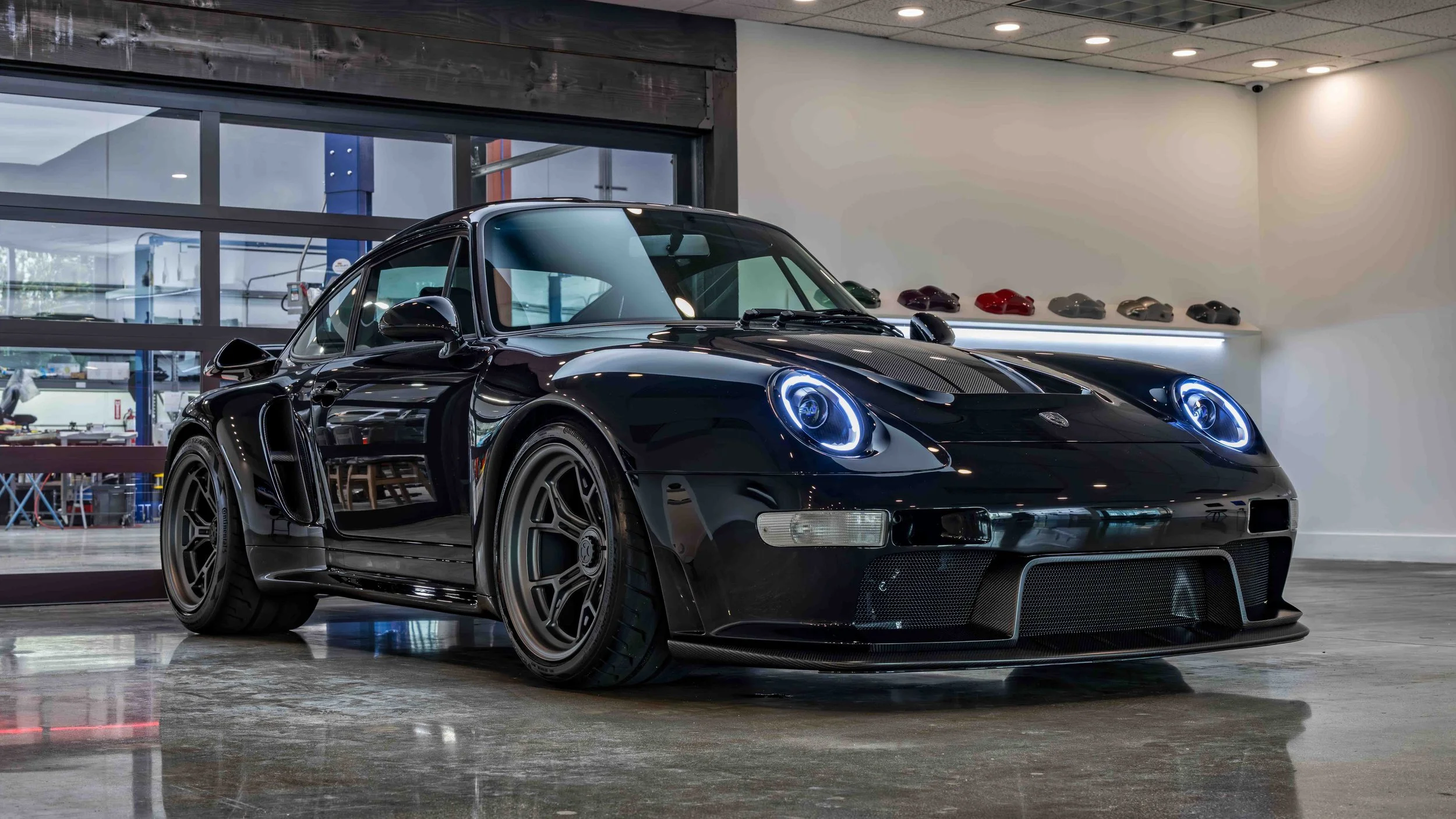 Turbo Florio 5 — NVIDIA Black Metallic 1996 Gunther Werks remastered Porsche 911 Turbo (993) parked in the Gunther Werks showroom, right front‑three‑quarter view with exposed carbon-fiber stripe and 18" Magnesium wheels. — #TurboFlorio5
