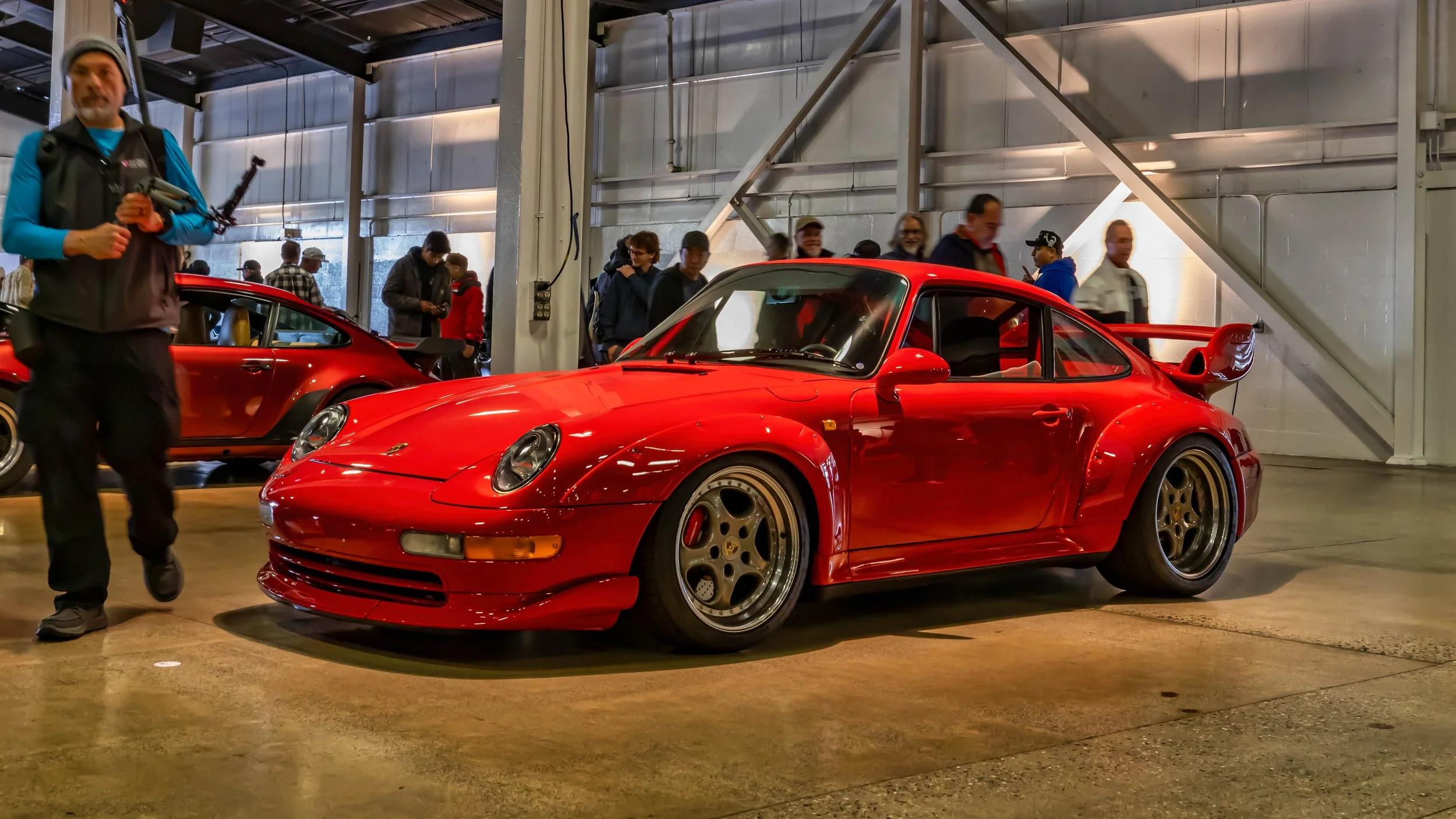 Air | Water 2025 — Orange County Fairgrounds — A red Porsche 911 GT2 (993) is displayed at an indoor car event, parked on a polished concrete floor. The car is shown from a low front three-quarters angle, highlighting its riveted widebody fenders, a 
