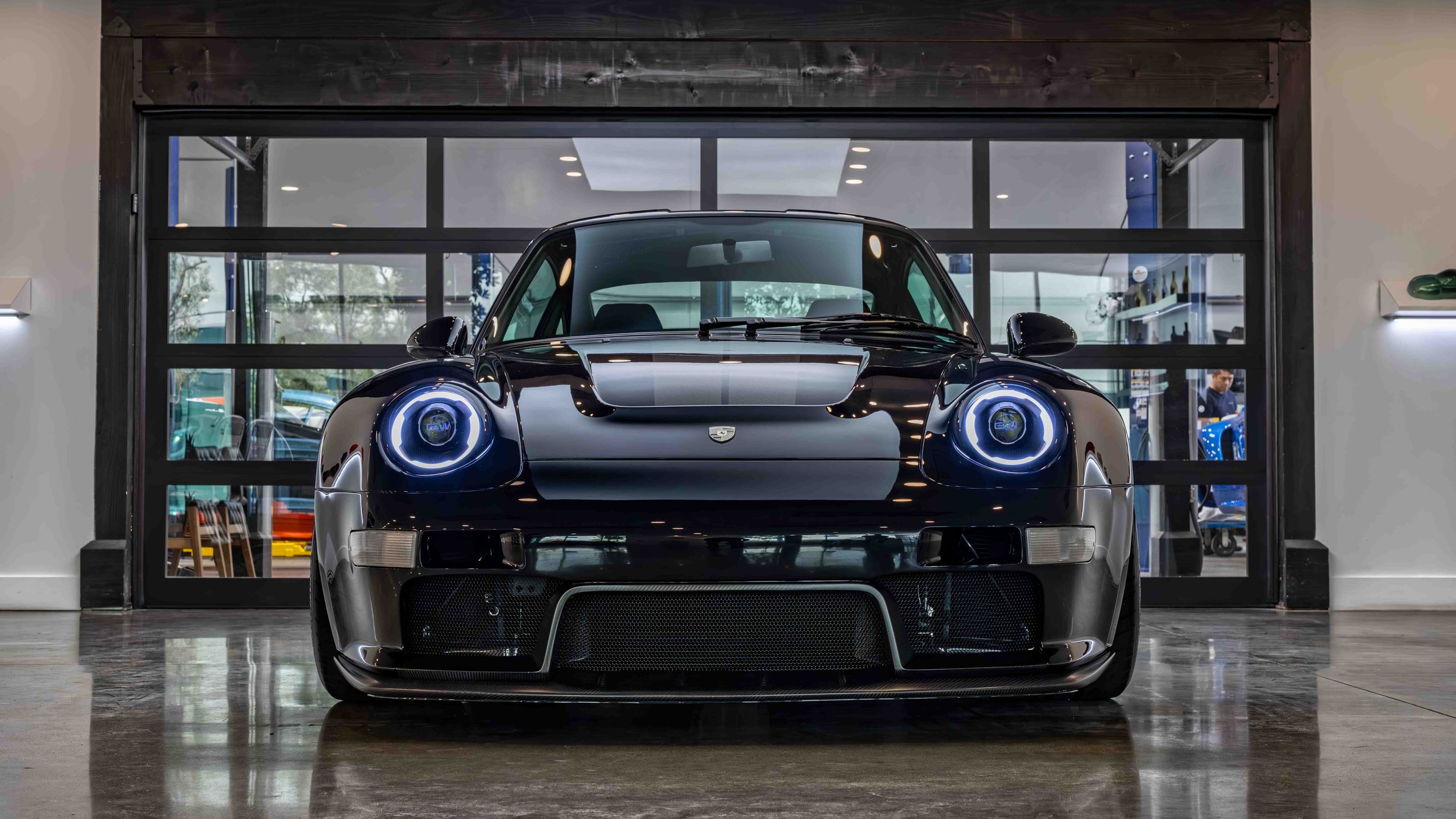 Turbo Florio 5 — NVIDIA Black Metallic 1996 Gunther Werks remastered Porsche 911 Turbo (993) parked in the Gunther Werks showroom, front‑view with exposed carbon-fiber stripe. — #TurboFlorio5
