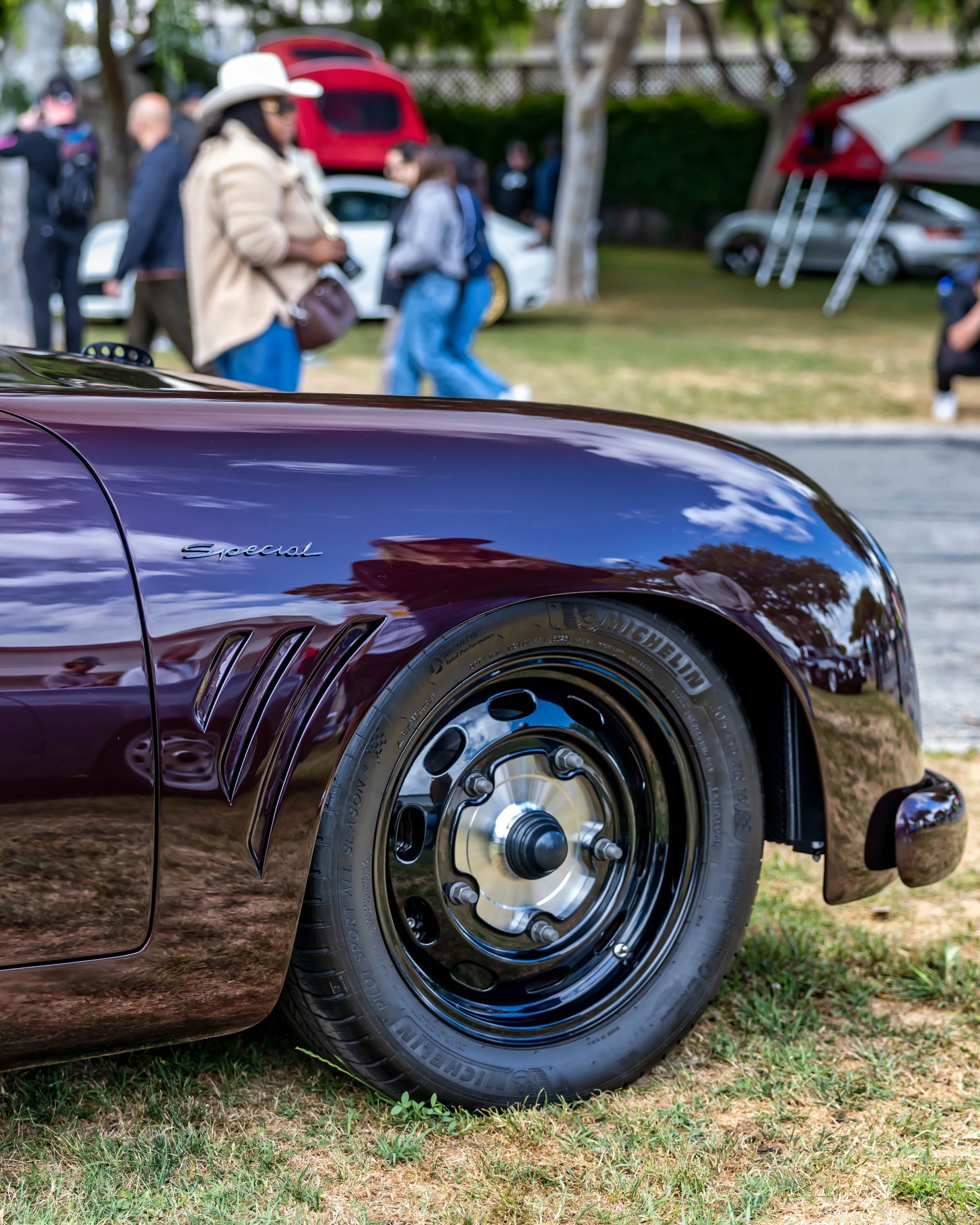 Air | Water 2025 — Emory Motorsports — OC Fairgrounds — A low-angle, close-up view of the front driver's side fender and wheel of a custom Emory Outlaw Special, based on a Porsche 356. The car is painted a deep metallic purple and features distinctiv