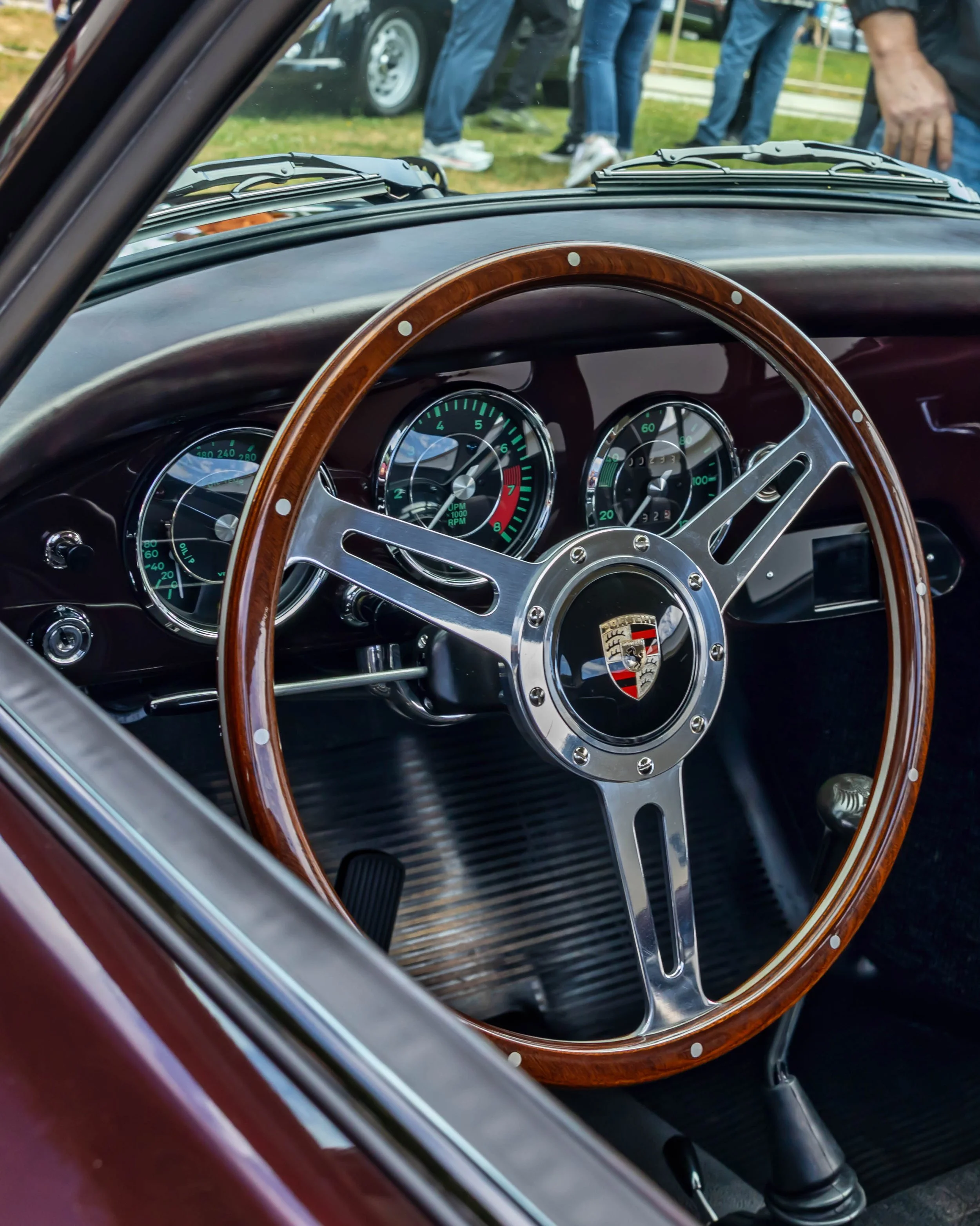 Air | Water 2025 — Emory Motorsports — OC Fairgrounds — A detailed interior shot of a vintage Porsche 356 Emory Outlaw Special, highlighting its classic wood and chrome steering wheel against a Superior Red Metallic dashboard. The green-on-black VDO 