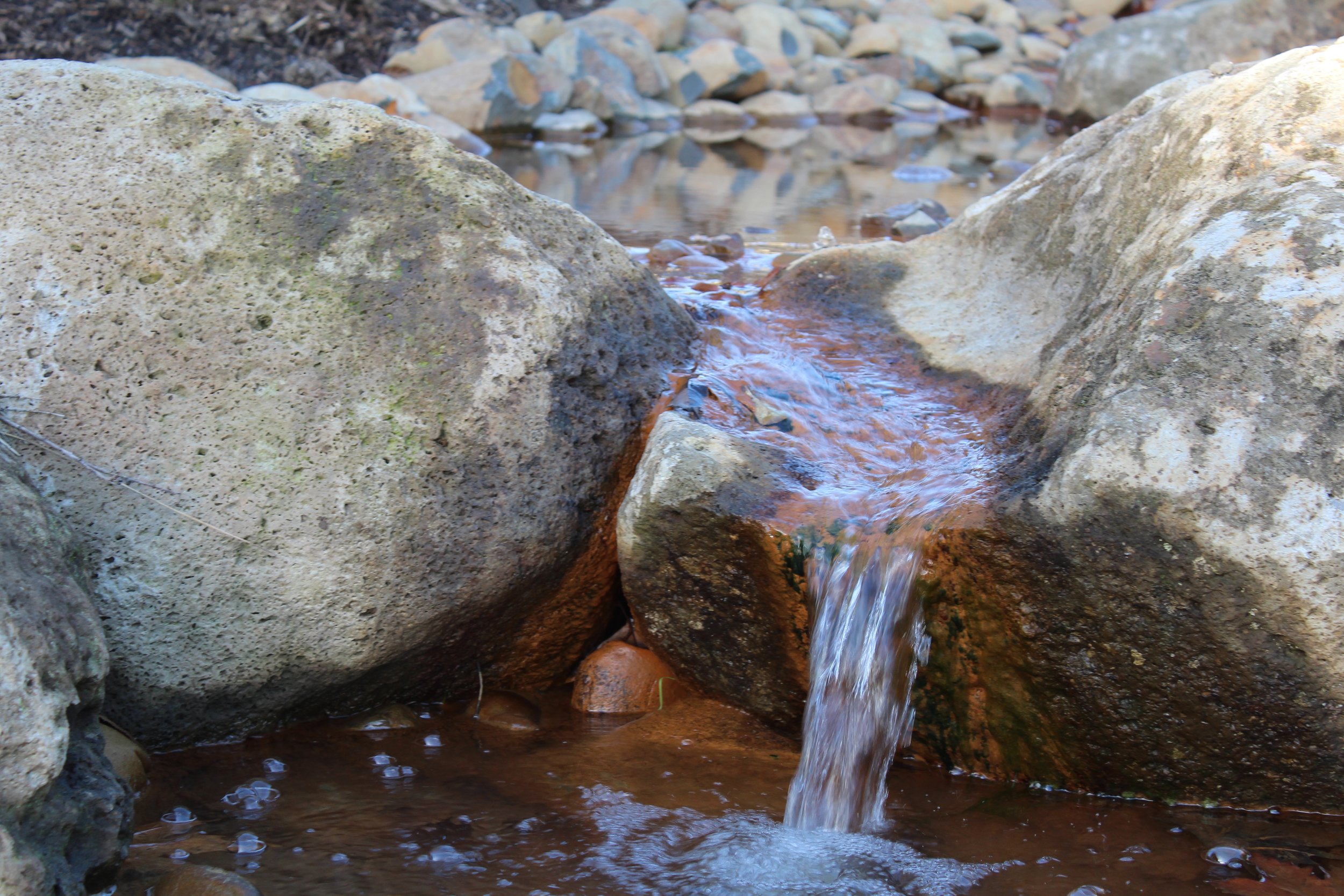 Small stream flowing between large rocks in a natural outdoor setting.