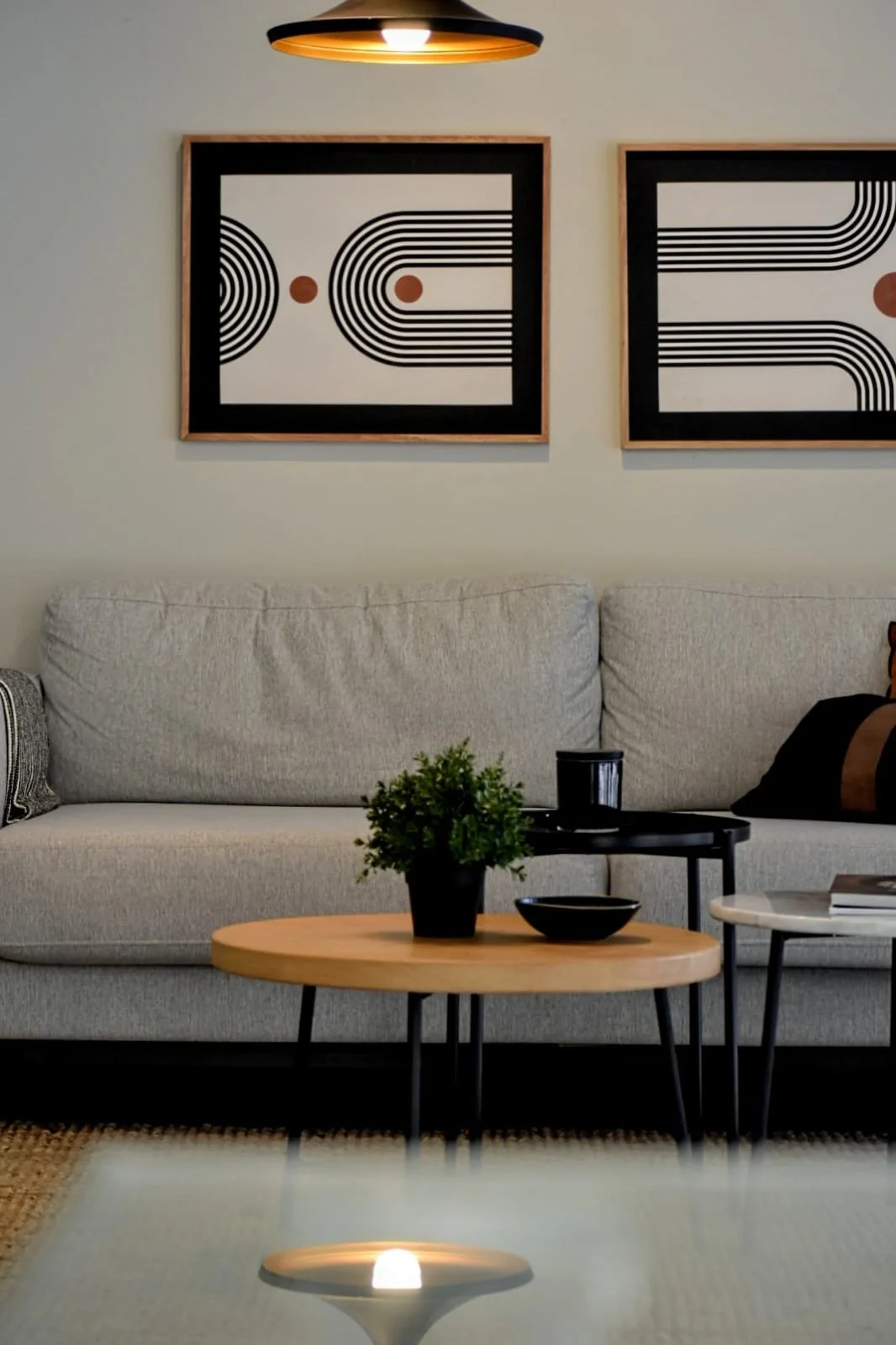 Sala moderna con sofá gris, mesas de centro de madera, arte geométrico en la pared y una lámpara colgante.