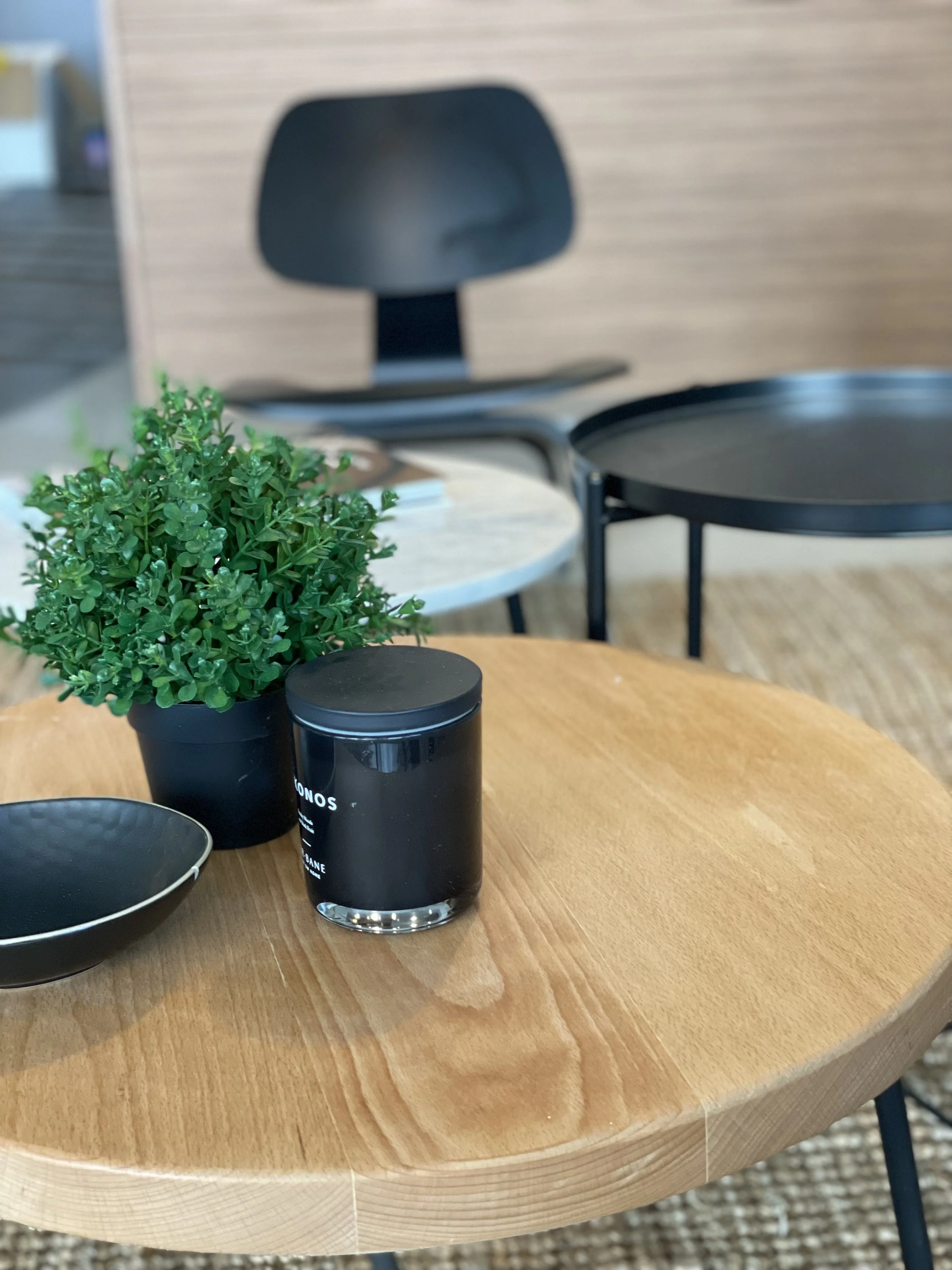 Mesa de madera con planta en maceta negra, vela negra y tazón, silla negra de fondo.