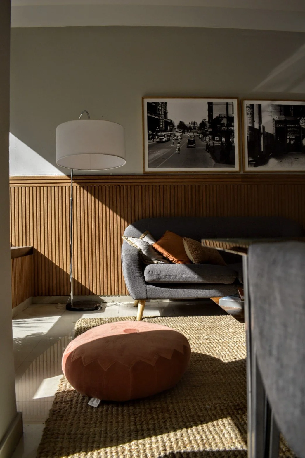 Sala de estar con un sofá gris, lámpara de pie blanca, cojines de colores, alfombra tejida y cuadros en blanco y negro en la pared.