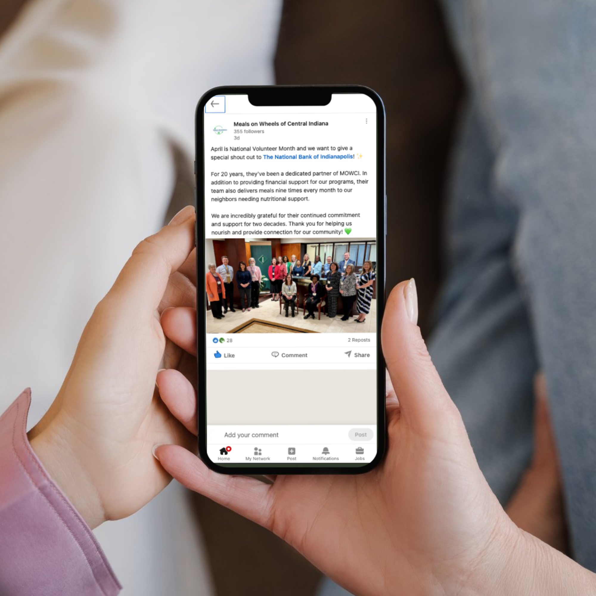 Person holding phone displaying a LinkedIn post from Meals on Wheels of Central Indiana that is recognizing a corporate volunteer group. 