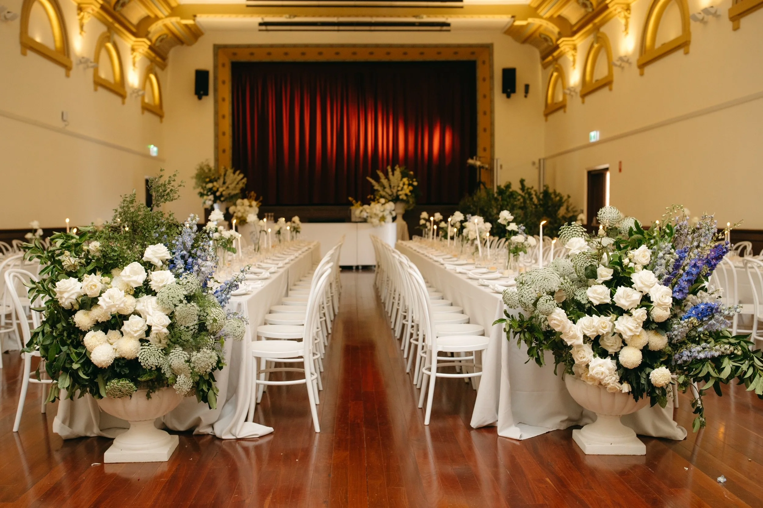 Deniliquin Town Hall wedding reception with long white tables, white bentwood chairs and abundant floral arrangements.
