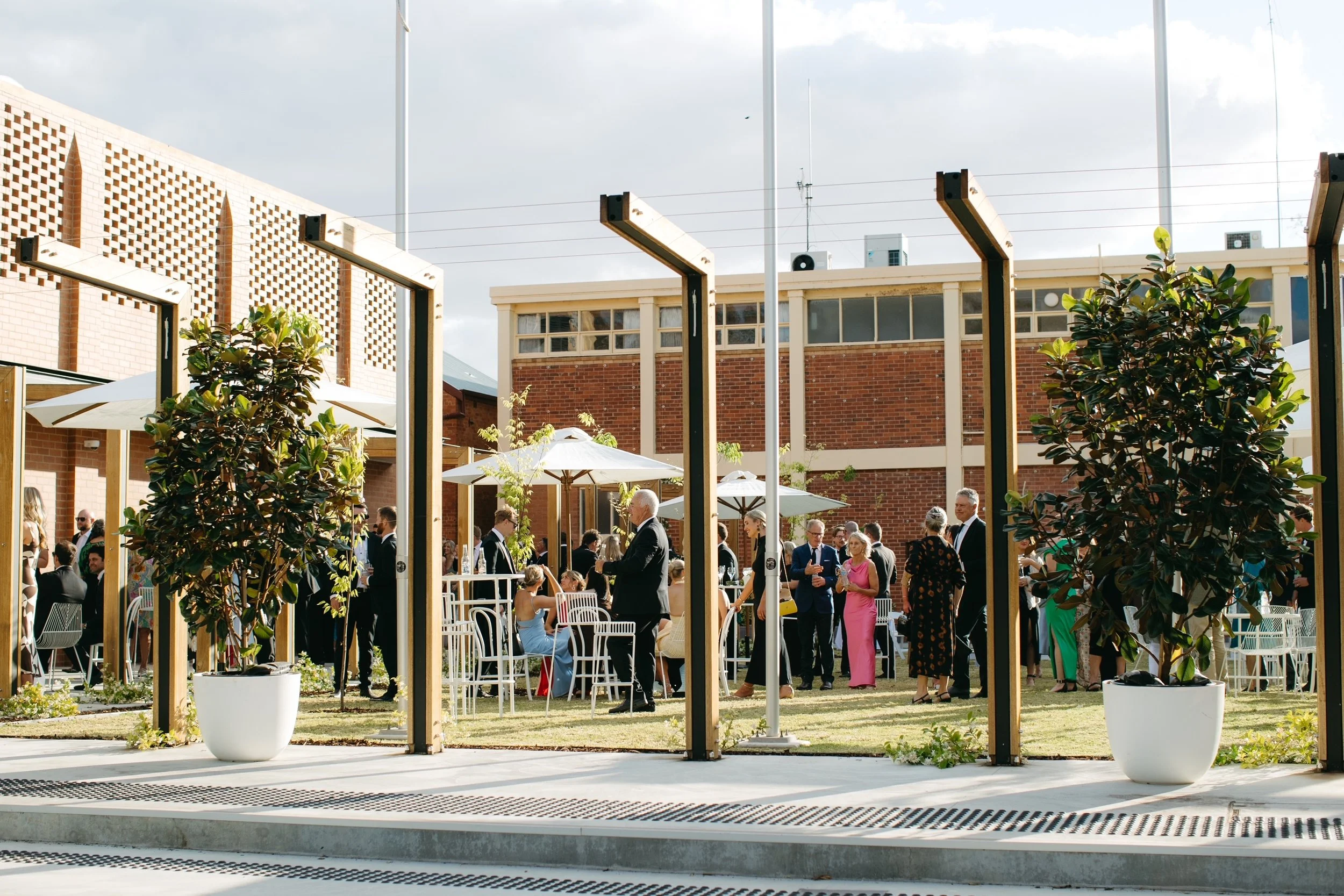 Outdoor wedding celebration at Deniliquin Town Hall with white furniture, umbrellas and guests gathering in the courtyard.