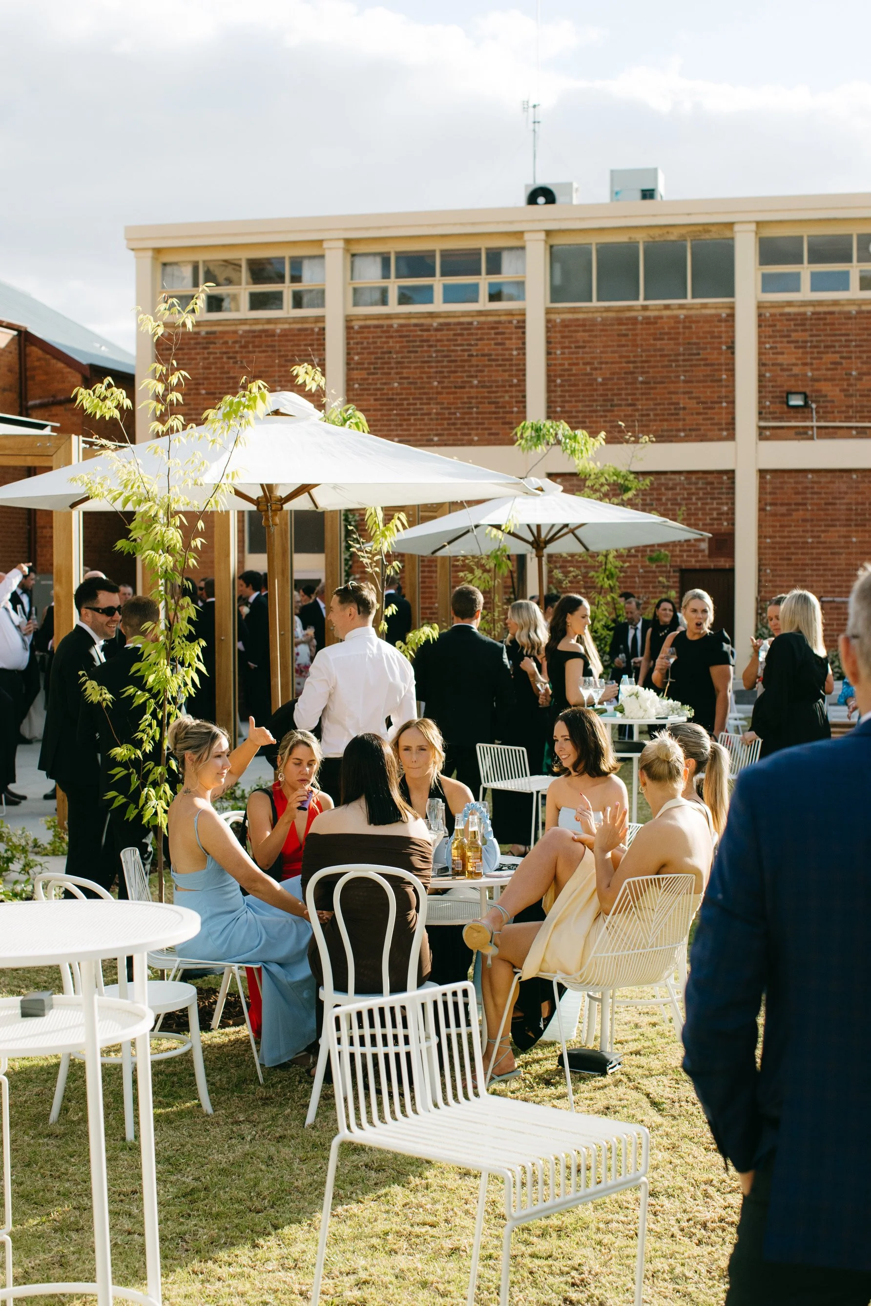 Wedding guests enjoying the outdoor courtyard with white event furniture and umbrellas at Deniliquin Town Hall.