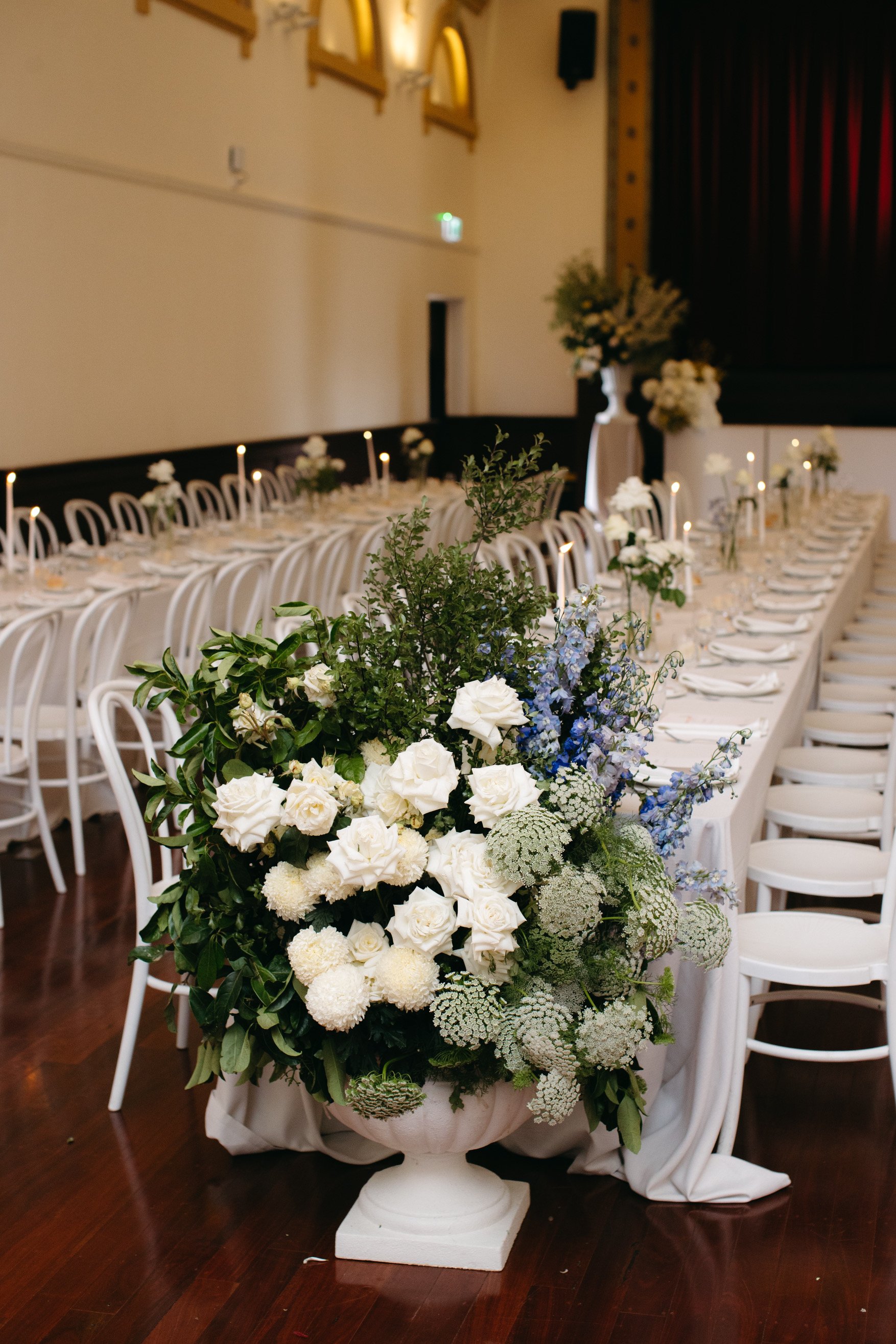 White and blue wedding florals framing long dining tables and white bentwood chairs at Deniliquin Town Hall.