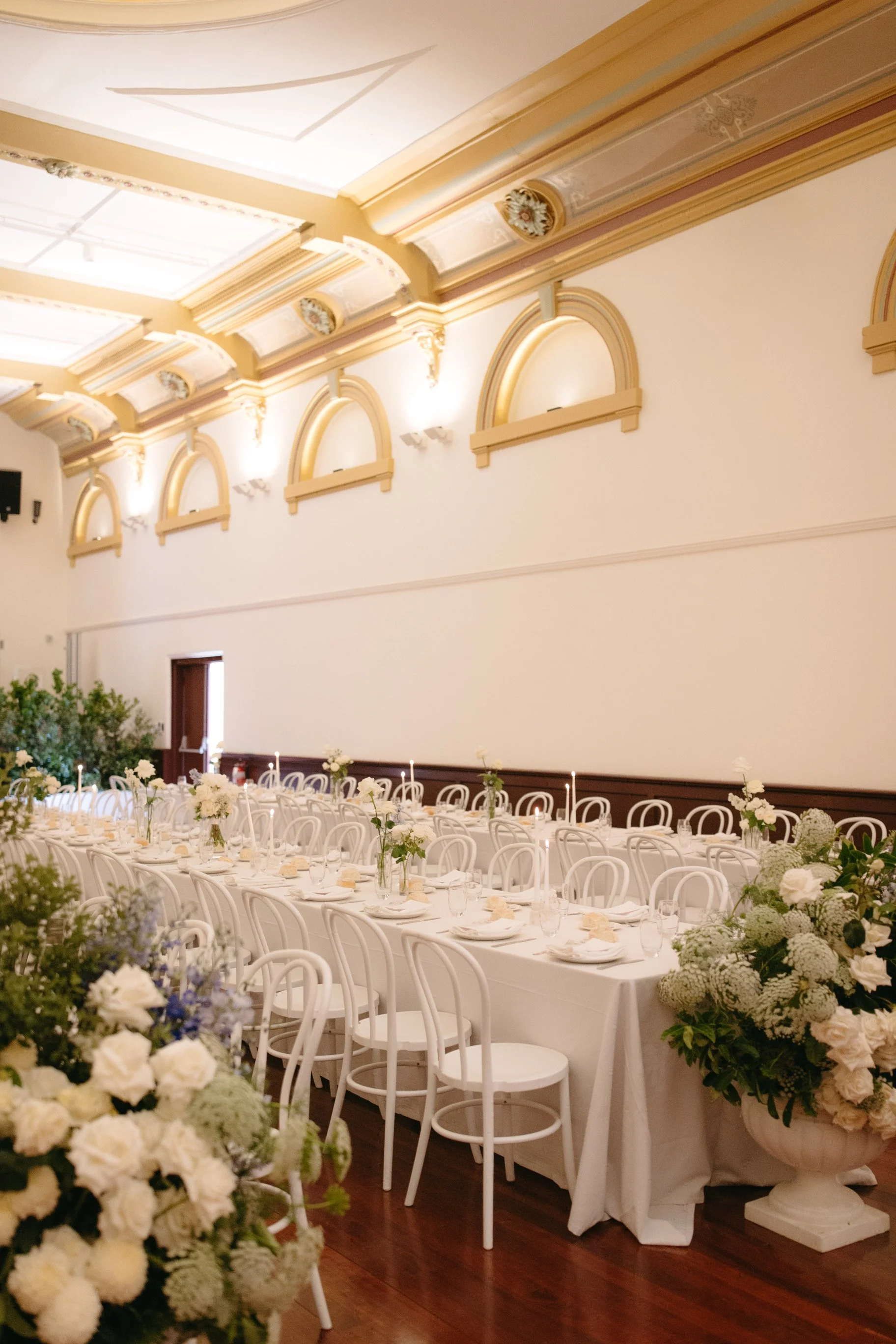 White bentwood chairs, long dining tables and floral arrangements inside Deniliquin Town Hall.