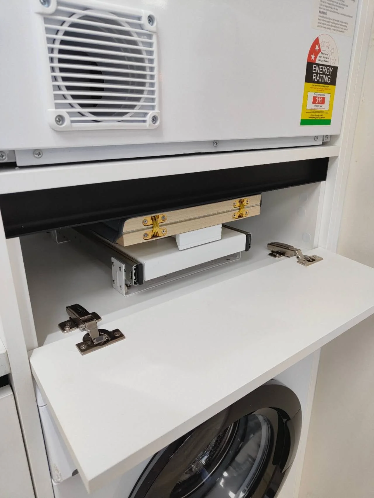 Built-in fold-down ironing board neatly stored inside a white laundry cabinet above a stacked washing machine and dryer.