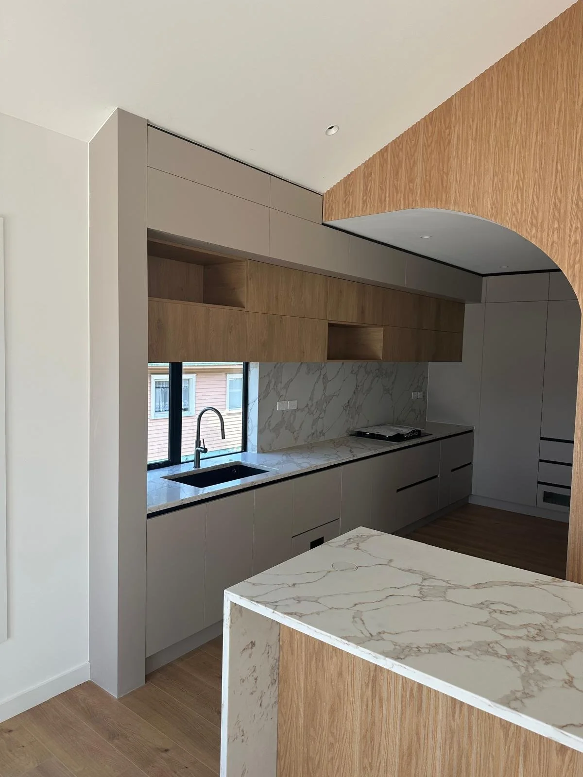 A sculptural modern kitchen featuring warm oak cabinetry, a curved island, marble-look stone surfaces and a striking curved timber wall panel.