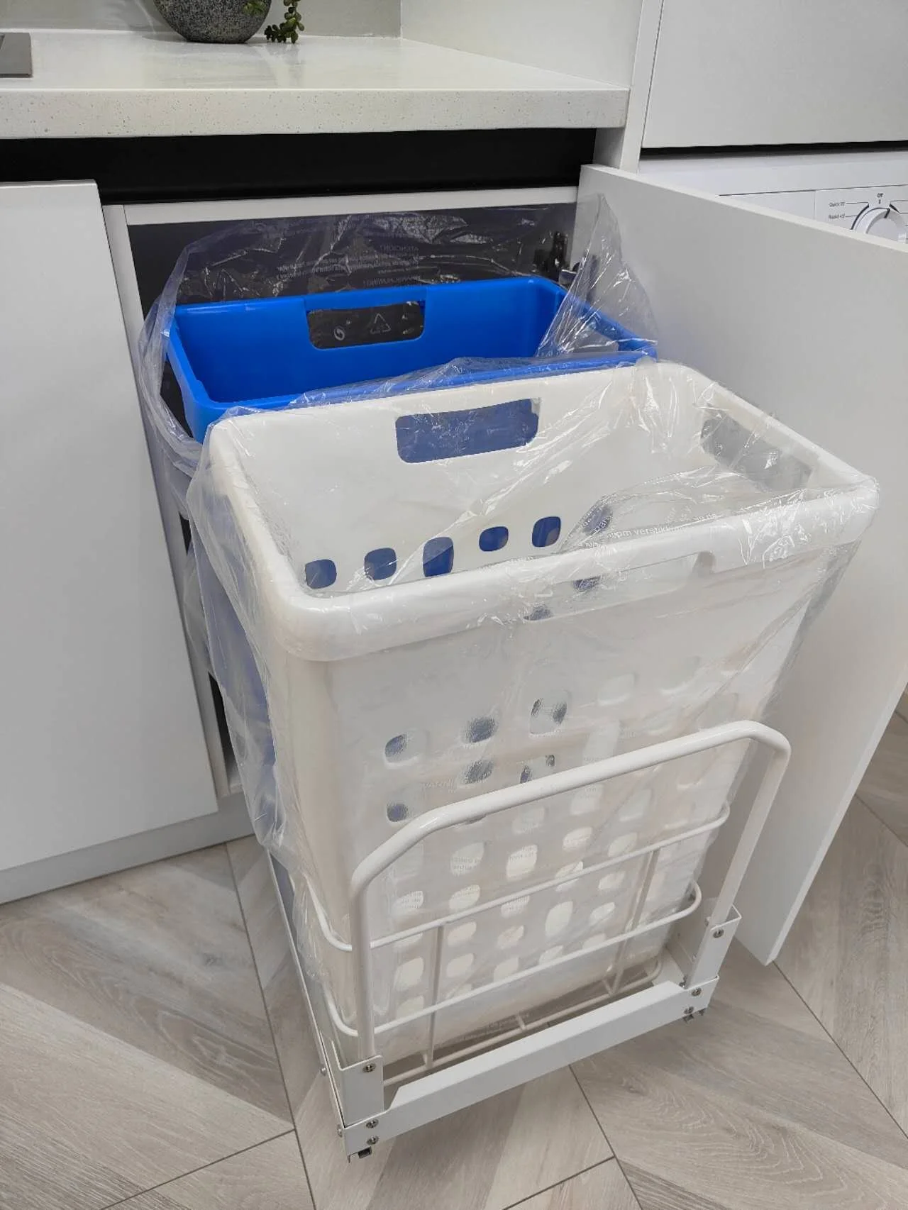 Double pull-out laundry hamper with removable washing baskets installed inside a modern white laundry cabinet.