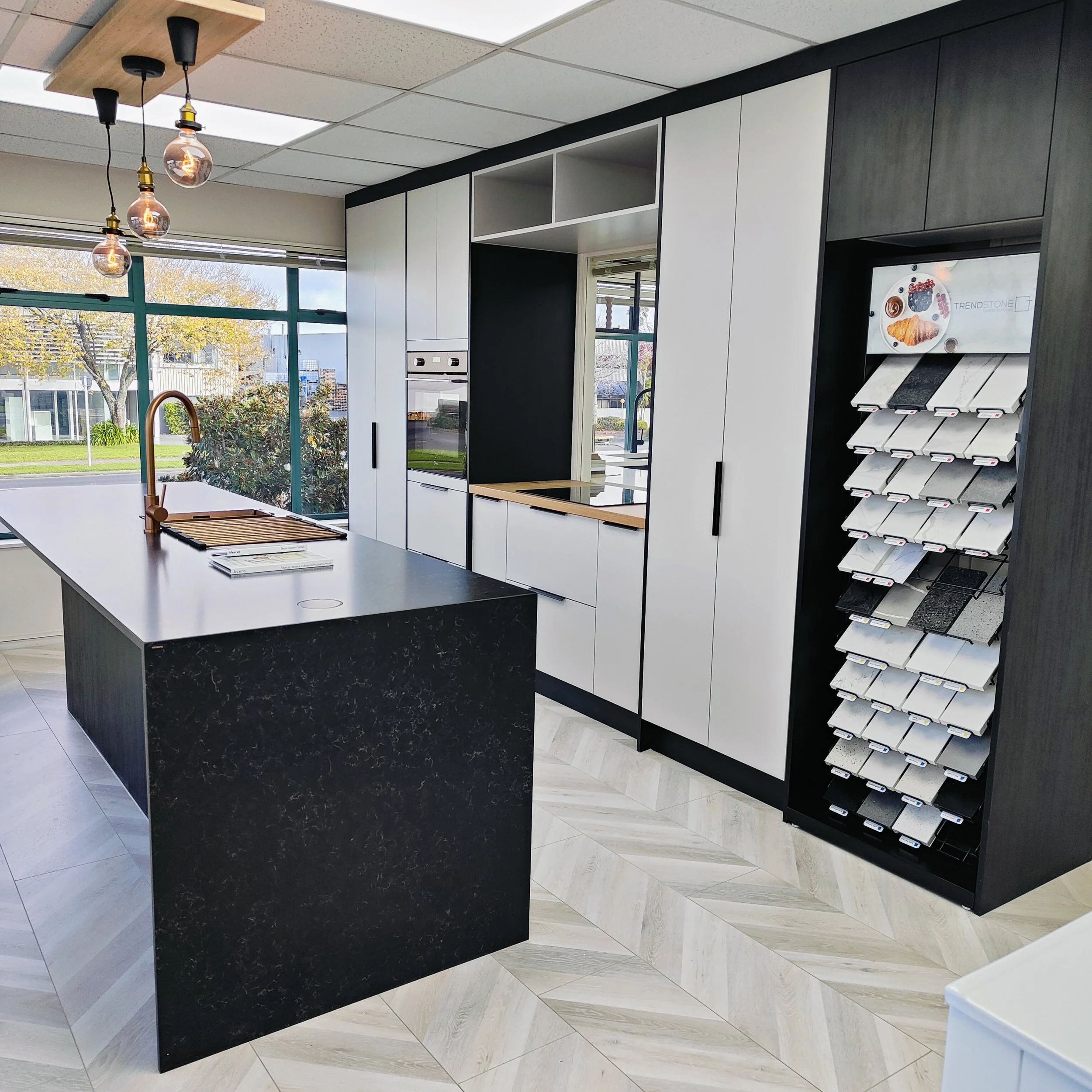 Customisable modern kitchen with a large black stone island benchtop, bar seating, light grey cabinetry, feature pendant lighting, and built-in appliances.