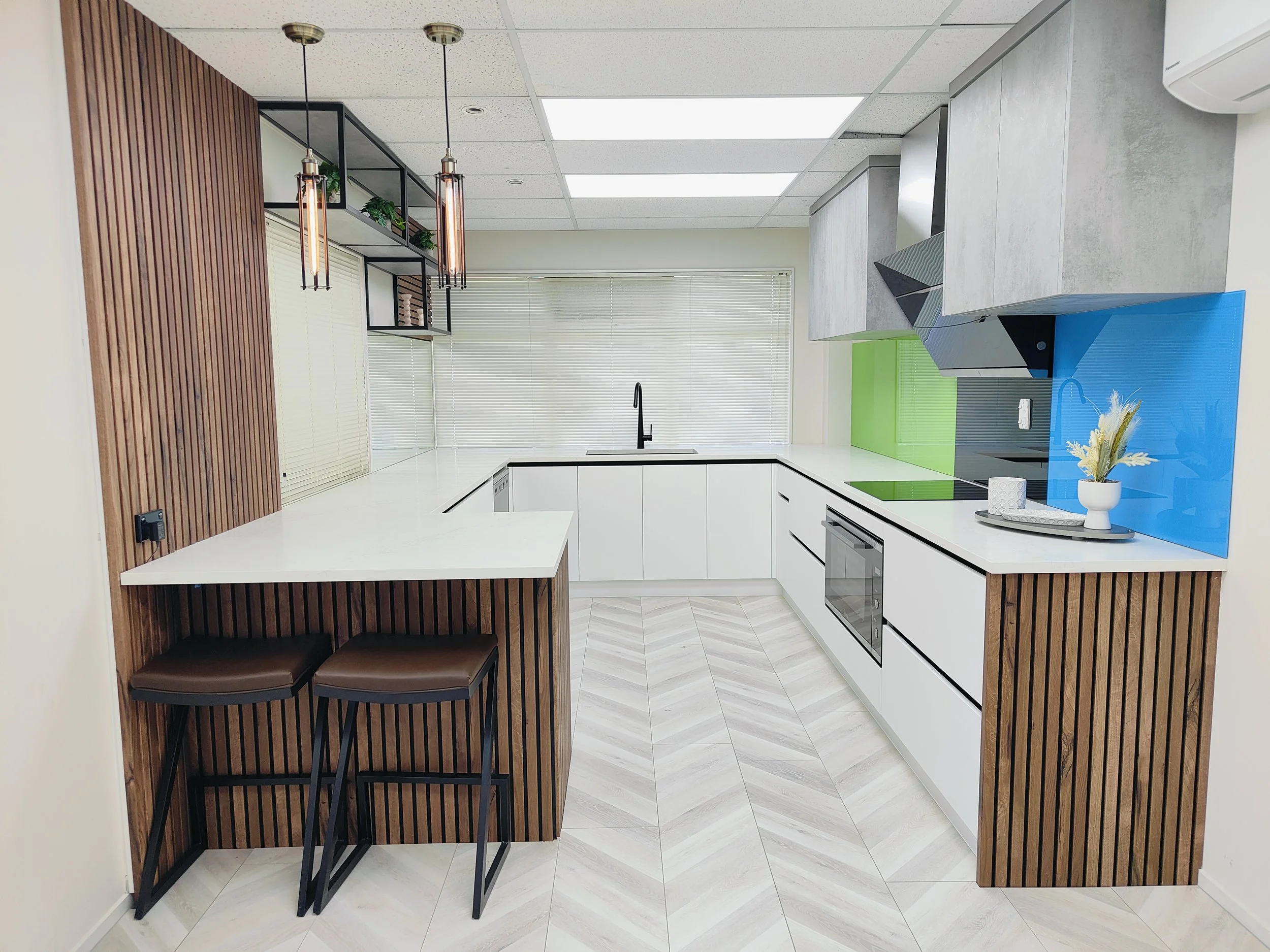 Customisable U-shaped kitchen with white cabinetry, timber feature panels, breakfast bar seating, and bold coloured glass splashbacks for a modern contrast.
