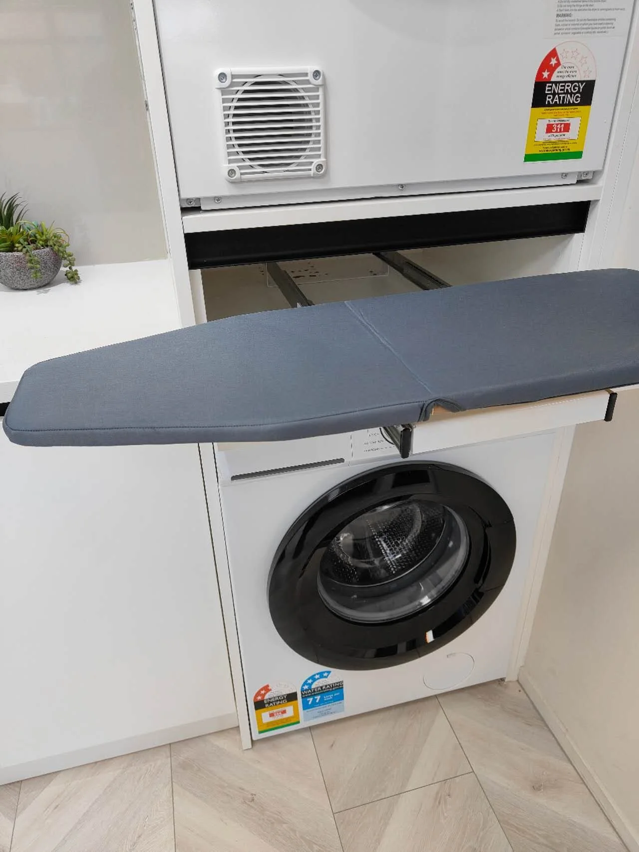 Pull-out fold-down ironing board extended from a modern white laundry cabinet for convenient laundry room ironing