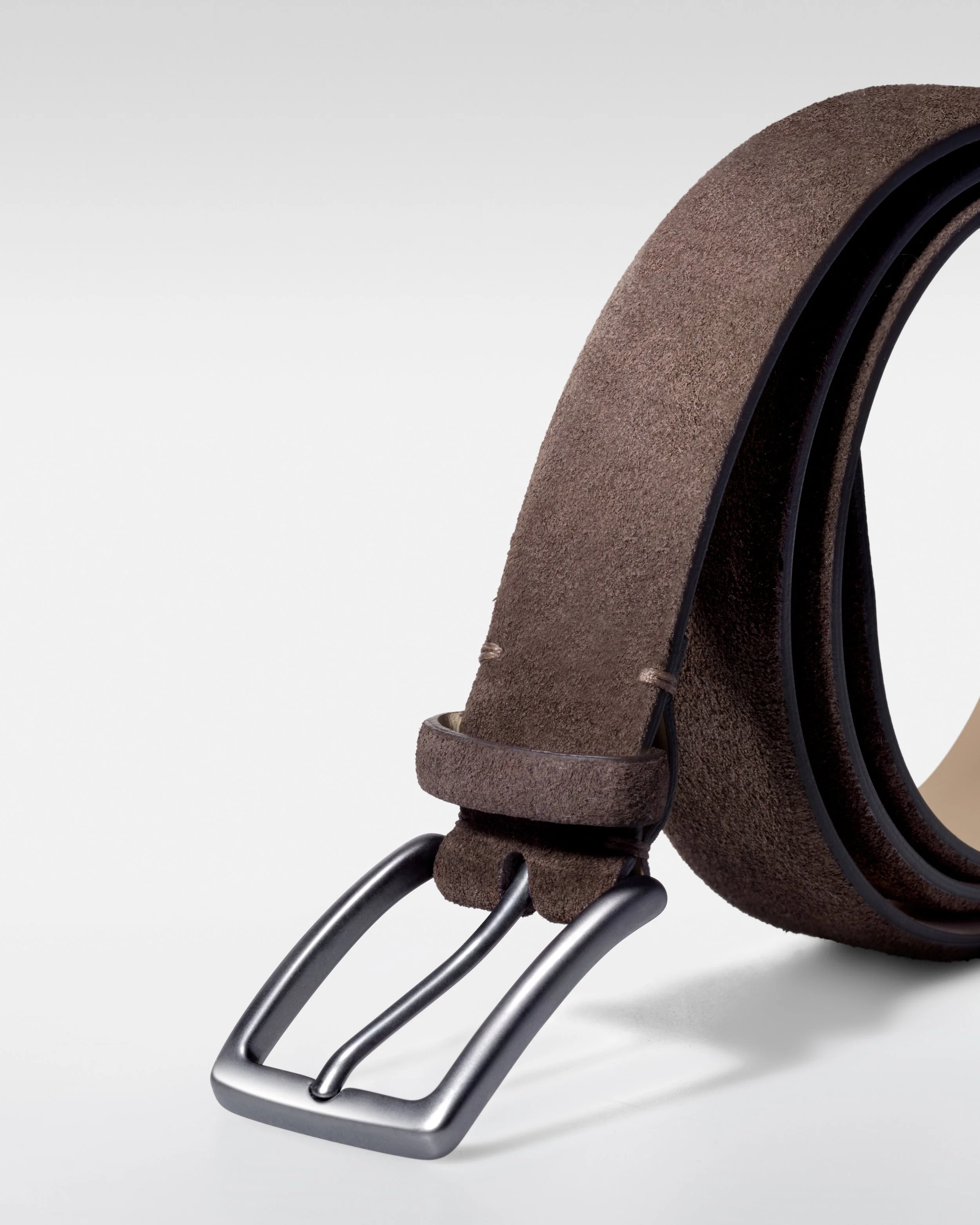 Close-up of a pair of black shoes with brown suede straps and metallic buckles, on a gray background.