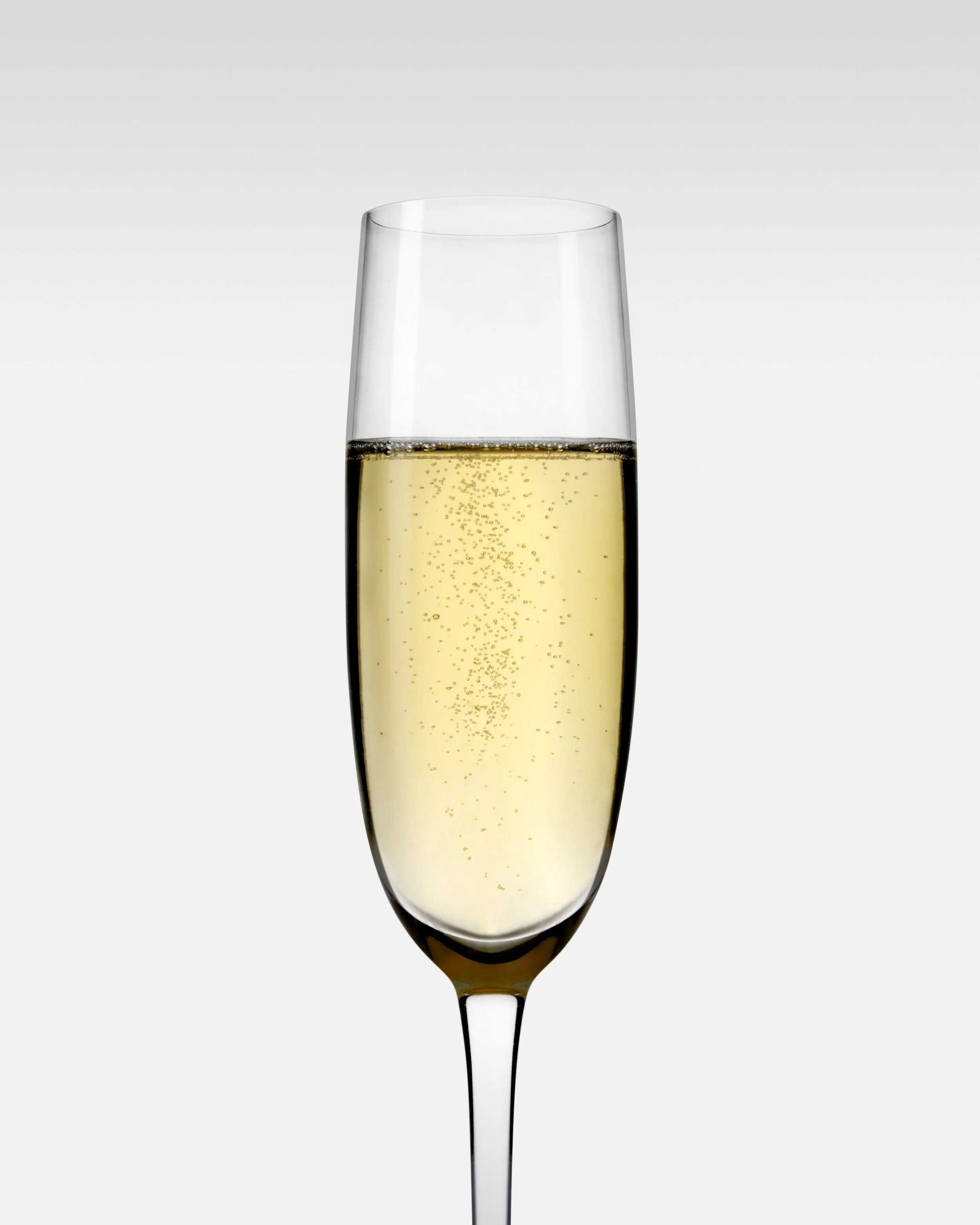 A tall champagne flute filled with sparkling white wine against a plain background.