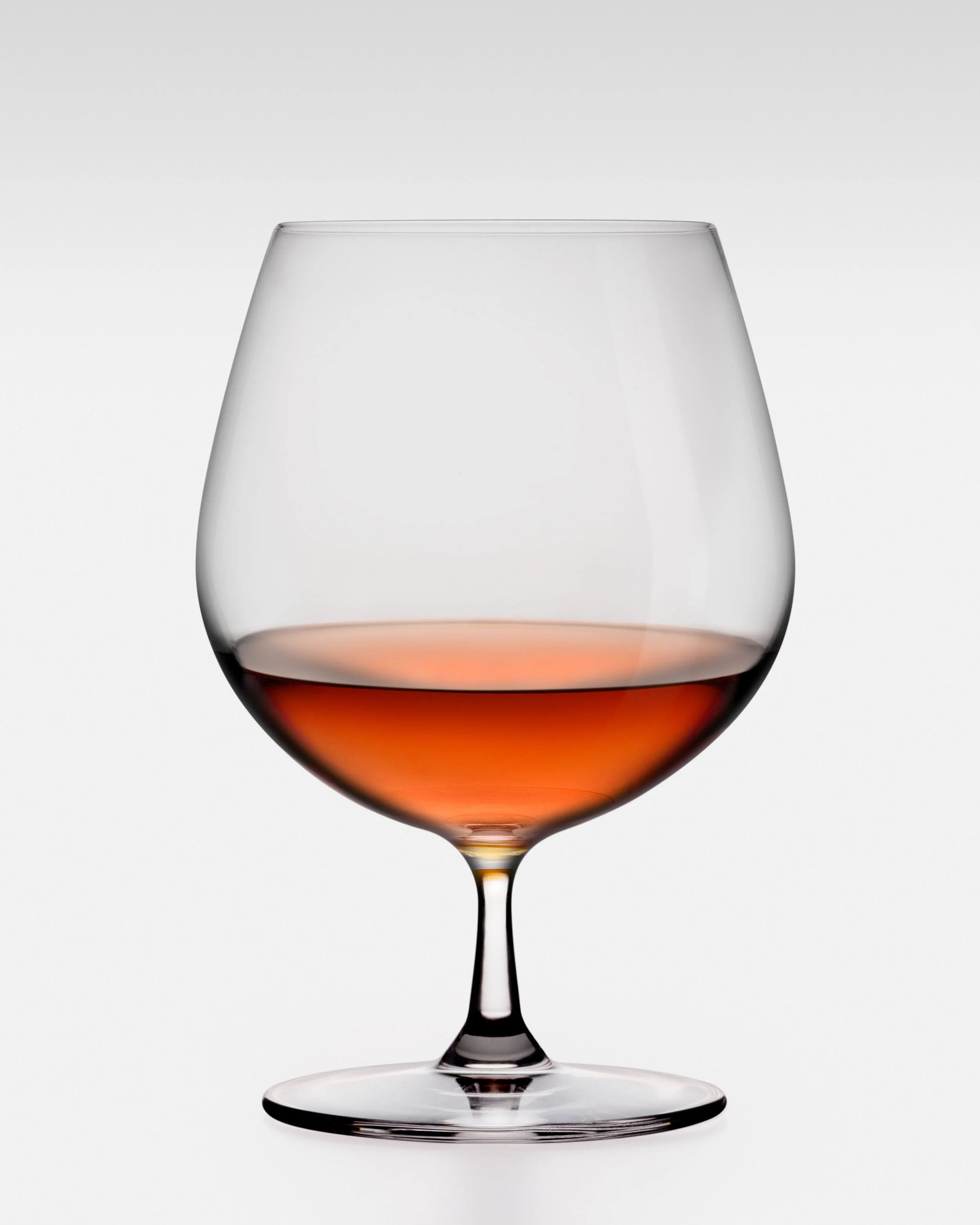 A glass of red wine with a transparent and reflective surface, set against a plain light gray background.