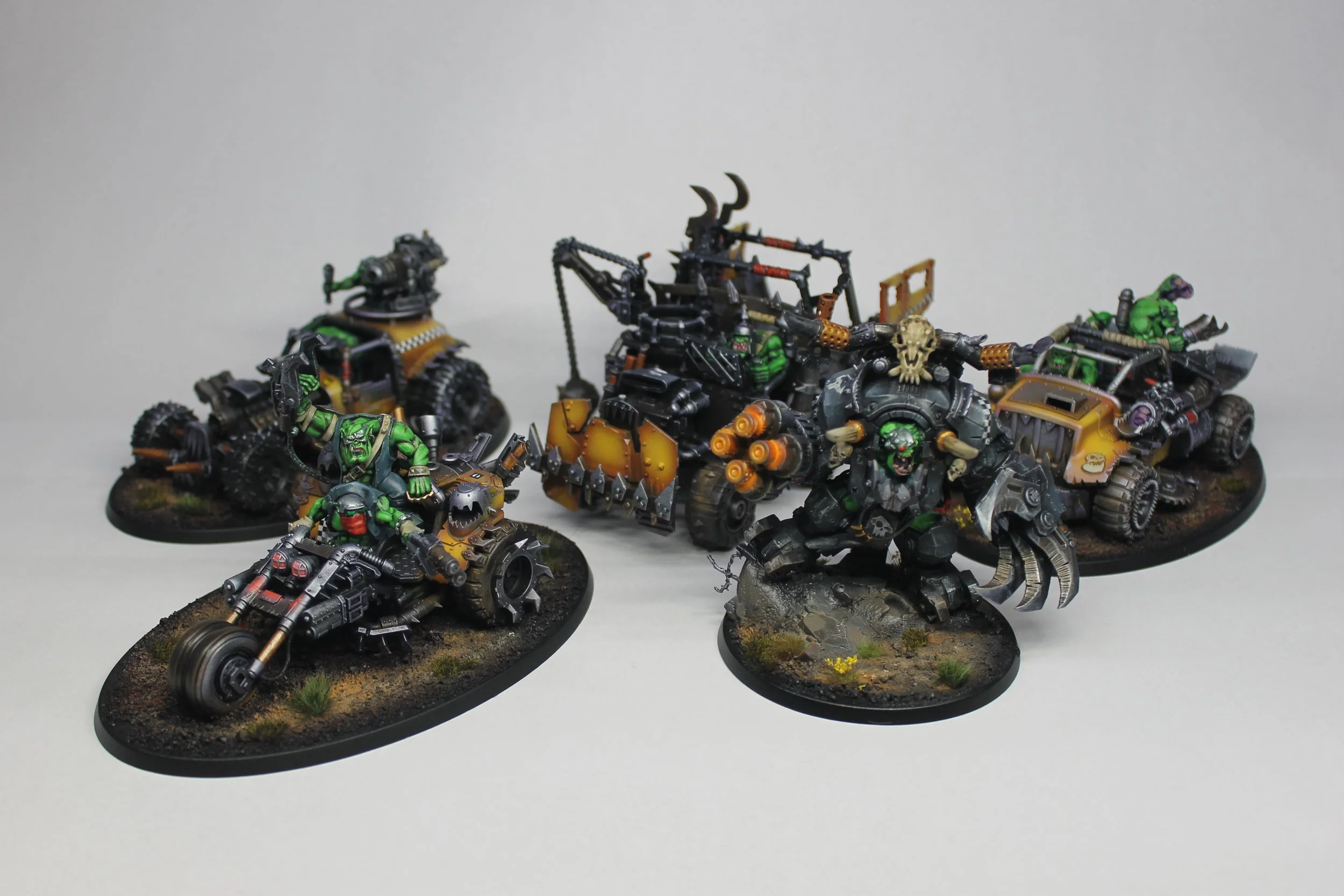 Collection of painted Warhammer miniatures, featuring orc-like figures with green skin, some in armor, weapons, and mechanical parts, with one large creature with an open mouth and monstrous appearance.