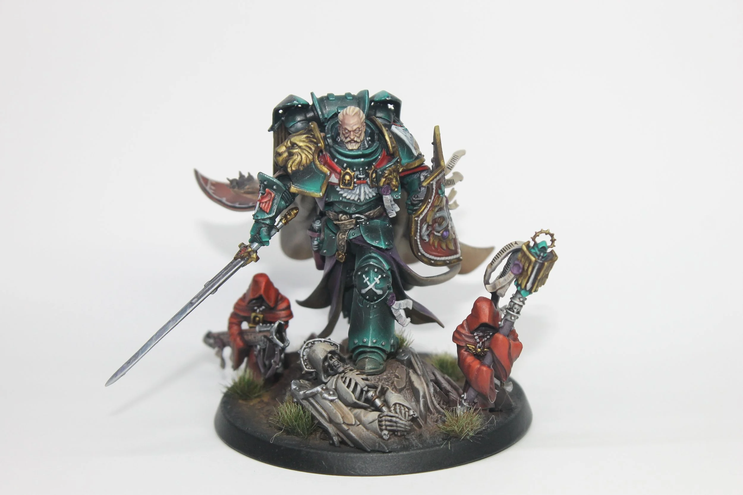 Detailed miniature model of a sci-fi armored warrior with a red cape, black and silver armor, holding a glowing green sword, standing on a rocky base with a flag bearing a skull and flames, in a dark setting.