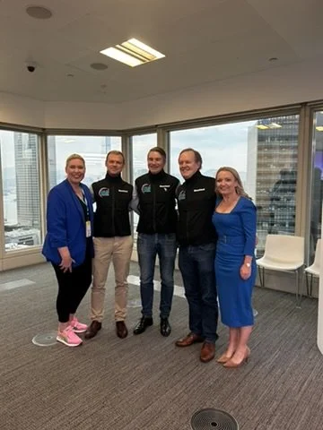 Five people standing in a high-rise office with large windows, cityscape view, and modern interior.