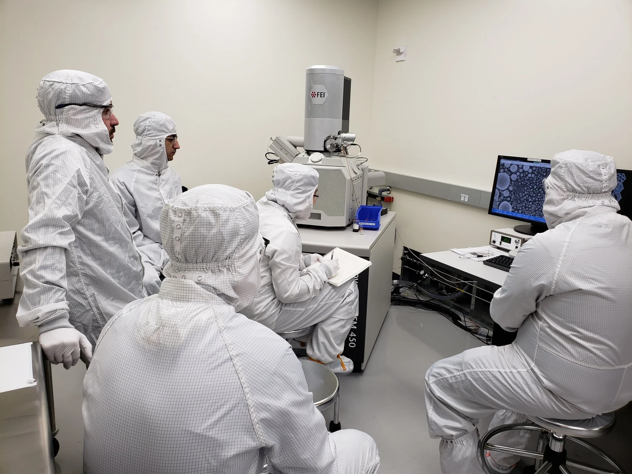 Group of users in cleanroom attire receiving training from staff on operating the Scanning Electron Microscope (SEM), focusing on nanoscale imaging techniques.