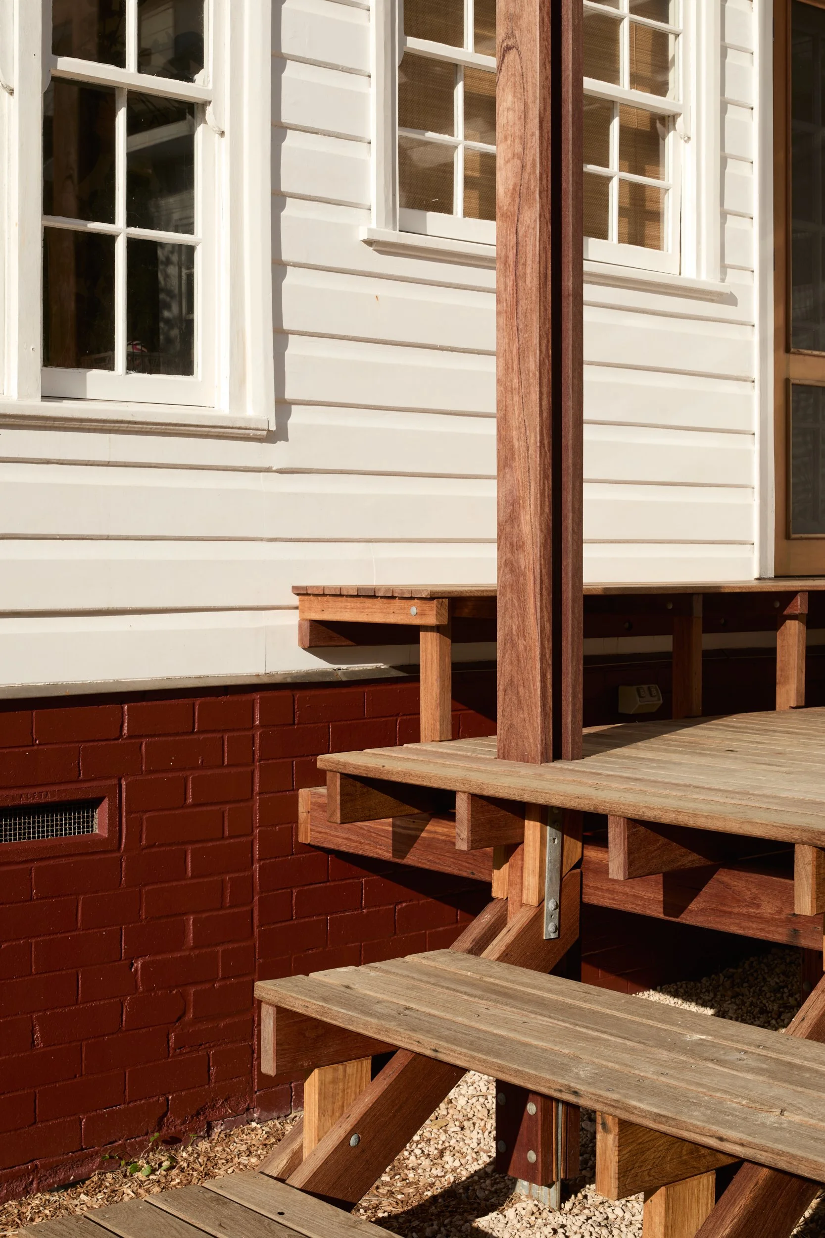 Exterior of a house with white siding and windows, a brick foundation, and a wooden deck with stairs.