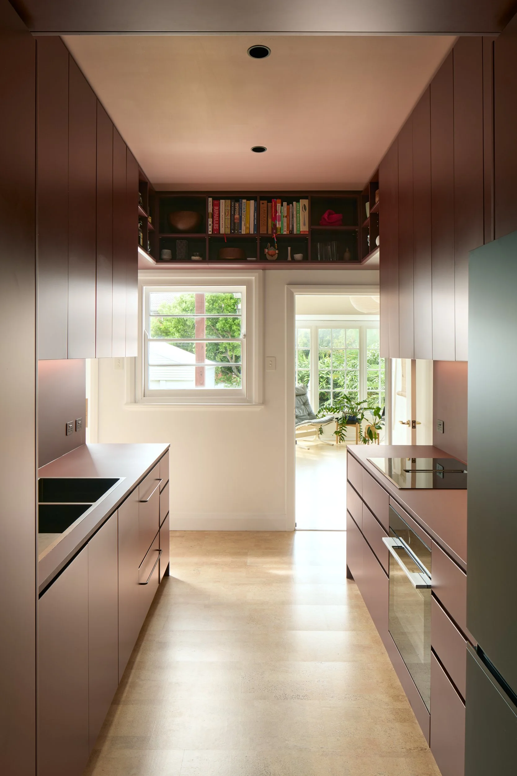 Modern kitchen with brown cabinets, wooden floors, and a view of a cozy sitting area with large windows and green plants.